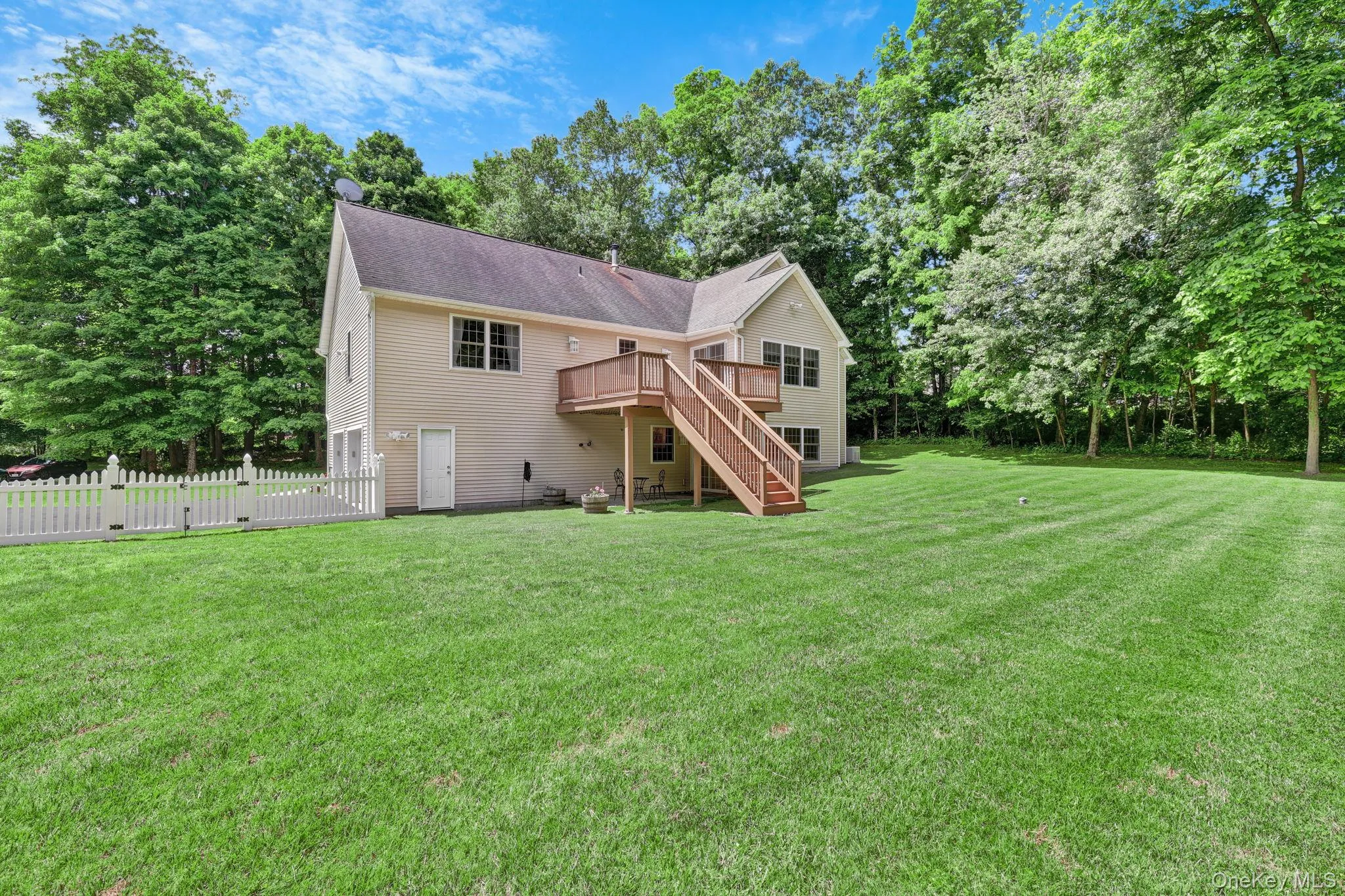Expansive rear yard featuring a large wooden deck, dual-stair access, and a white picket fence bordering the property Expansive rear yard featuring a large wooden deck, dual-stair access, and a white picket fence bordering the property