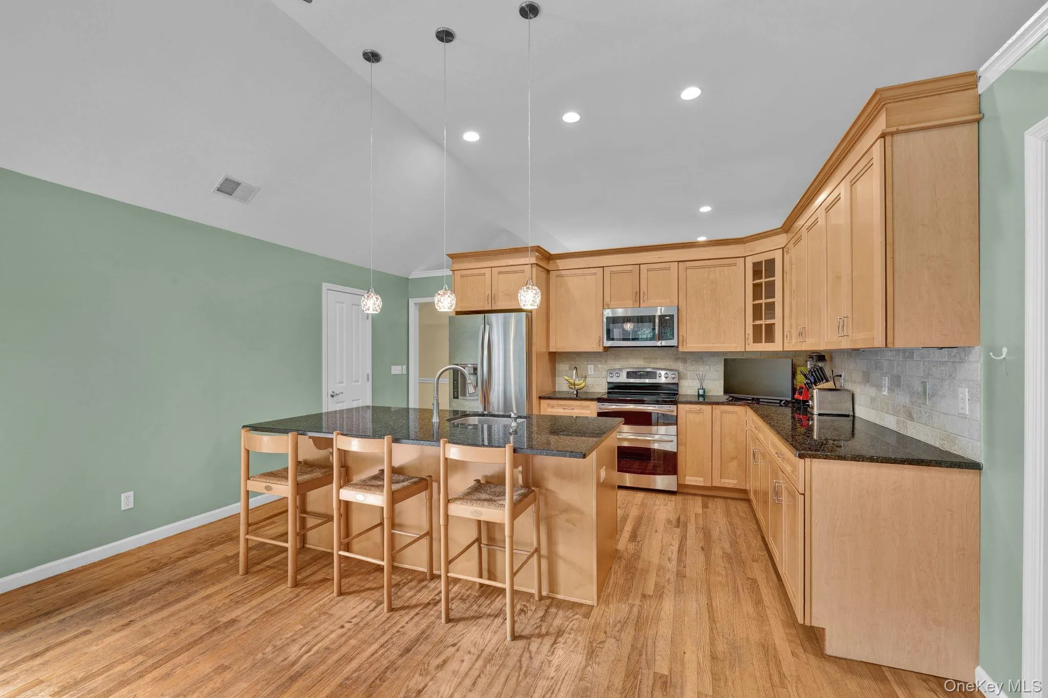 This huge, beautiful kitchen features a large central island with seating, stainless steel appliances, light wood cabinetry, and wood-finish flooring This huge, beautiful kitchen features a large central island with seating, stainless steel appliances, light wood cabinetry, and wood-finish flooring
