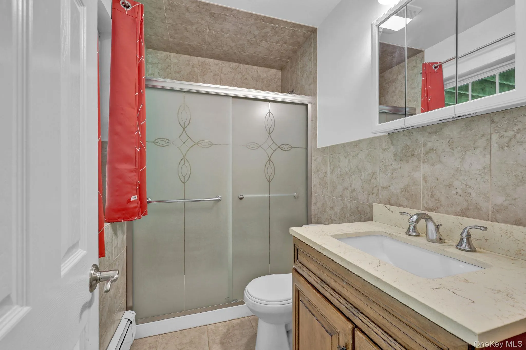Full bathroom downstairs featuring a walk-in shower with patterned sliding glass shower closure, full wall tile surround, vanity with an integrated sink, polished chrome faucet, and a wall-mounted medicine cabinet Full bathroom downstairs featuring a walk-in shower with patterned sliding glass shower closure, full wall tile surround, vanity with an integrated sink, polished chrome faucet, and a wall-mounted medicine cabinet