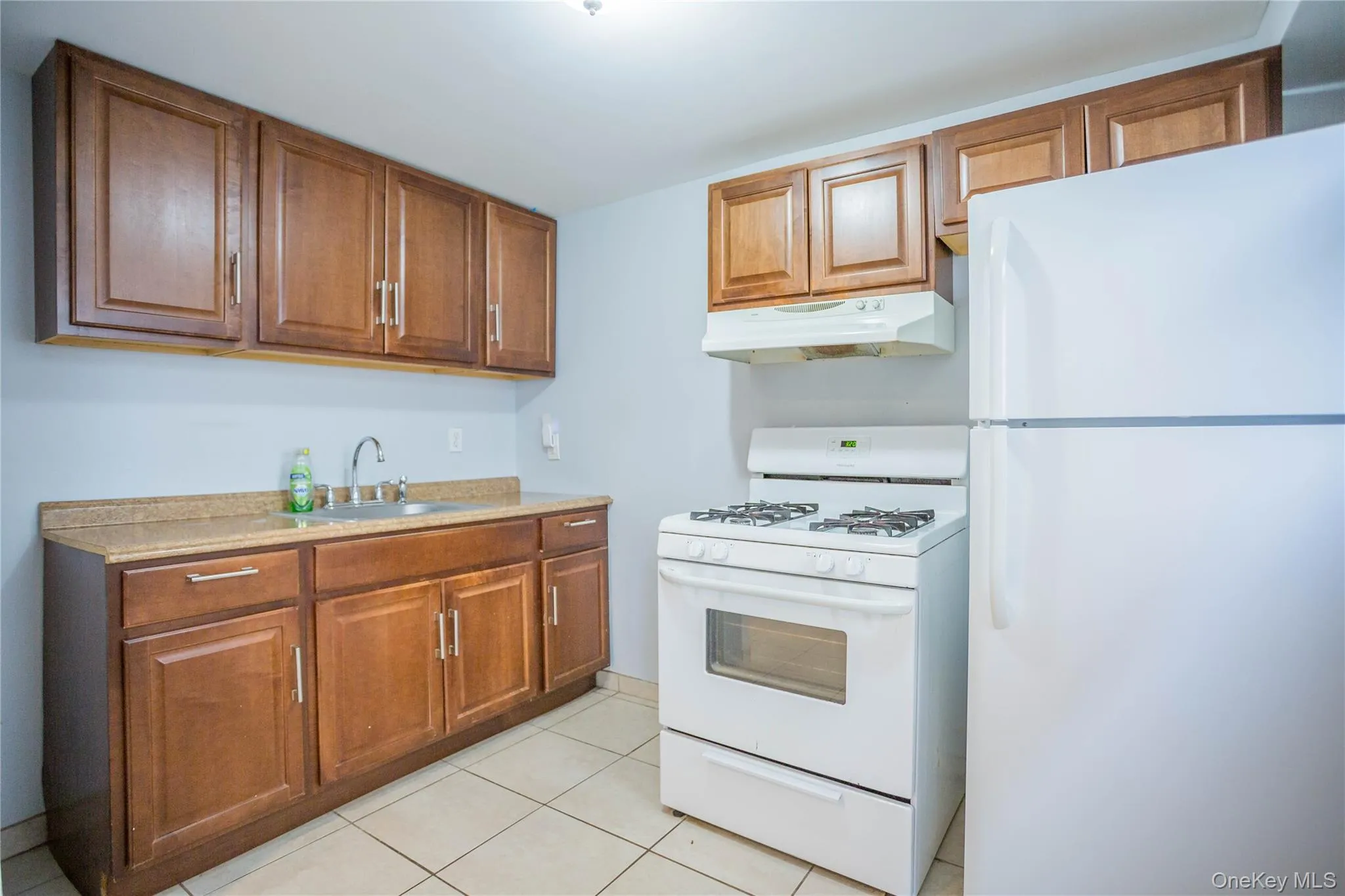 Kitchen featuring brown cabinetry, under cabinet range hood, white appliances, and a sink Kitchen featuring brown cabinetry, under cabinet range hood, white appliances, and a sink