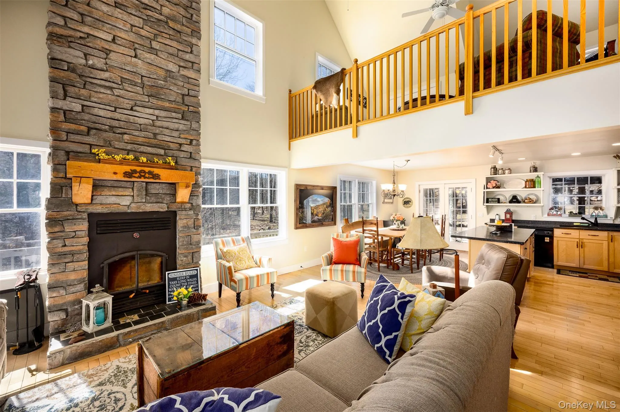 Living area featuring light wood-type flooring, healthy amount of natural light, a fireplace, and a high ceiling Living area featuring light wood-type flooring, healthy amount of natural light, a fireplace, and a high ceiling