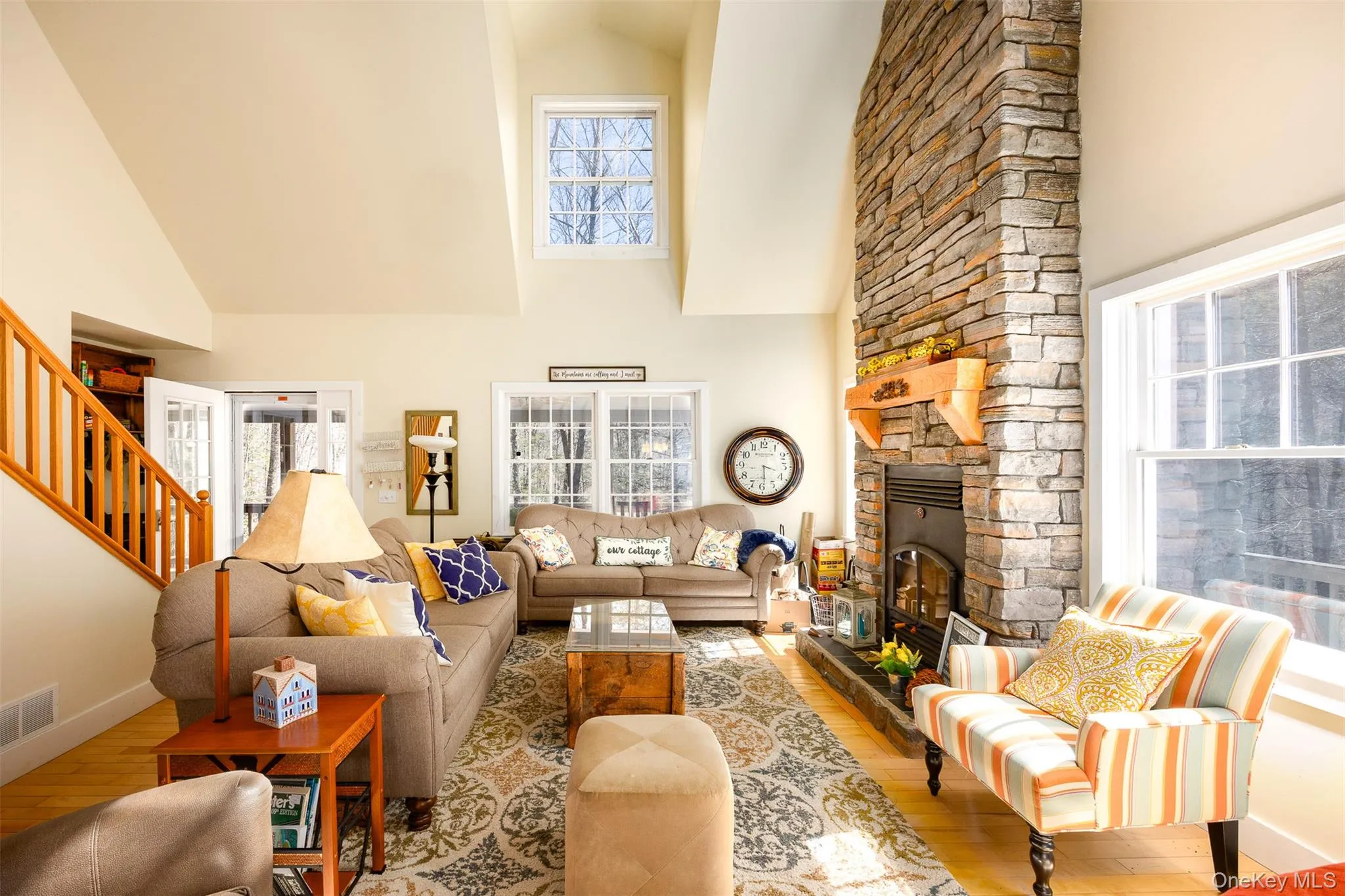 Living room with hardwood / wood-style flooring, a stone fireplace, and a high ceiling Living room with hardwood / wood-style flooring, a stone fireplace, and a high ceiling