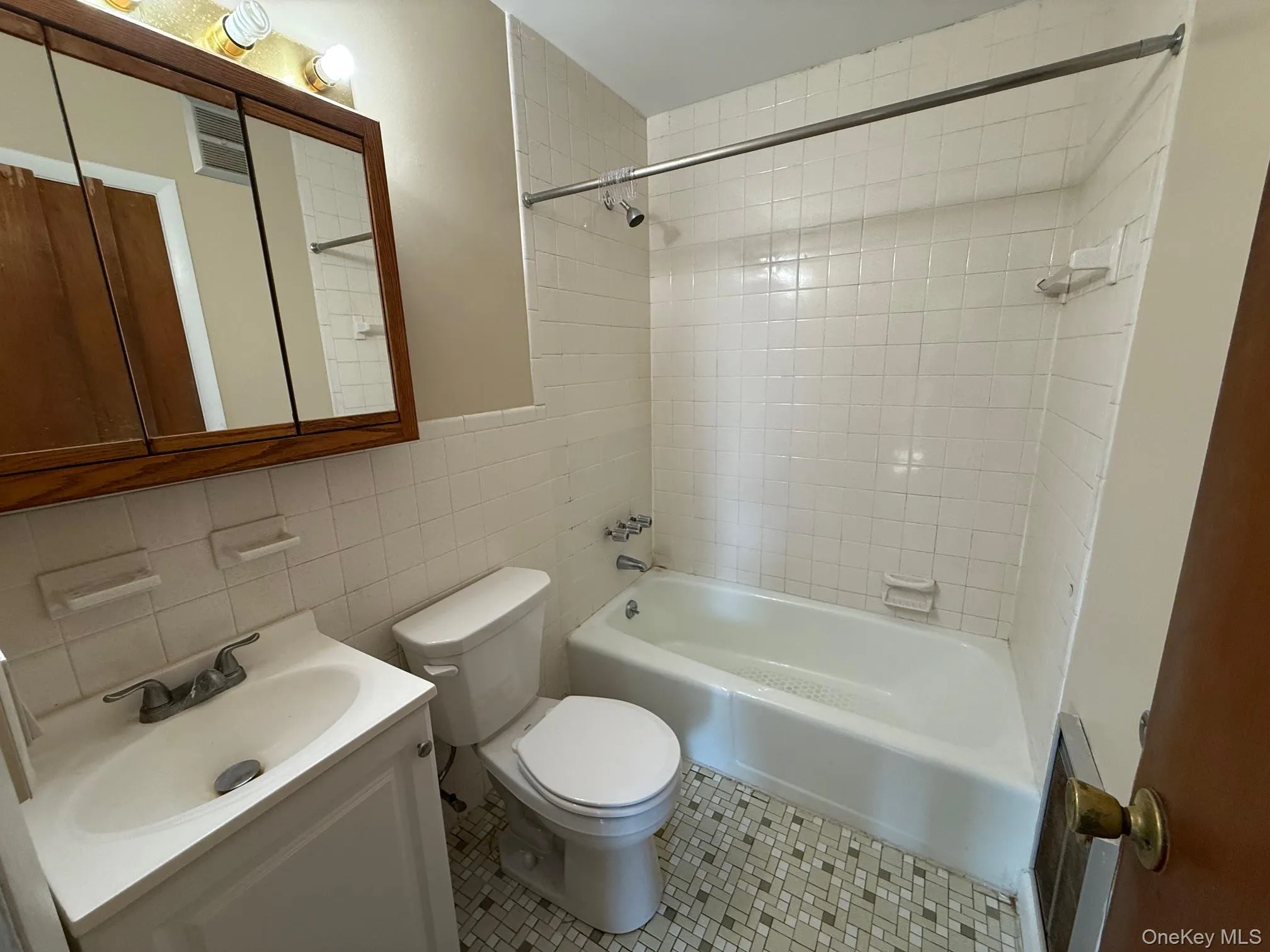 Full bathroom with tile walls, bathtub / shower combination, vanity, and tile patterned floors Full bathroom with tile walls, bathtub / shower combination, vanity, and tile patterned floors