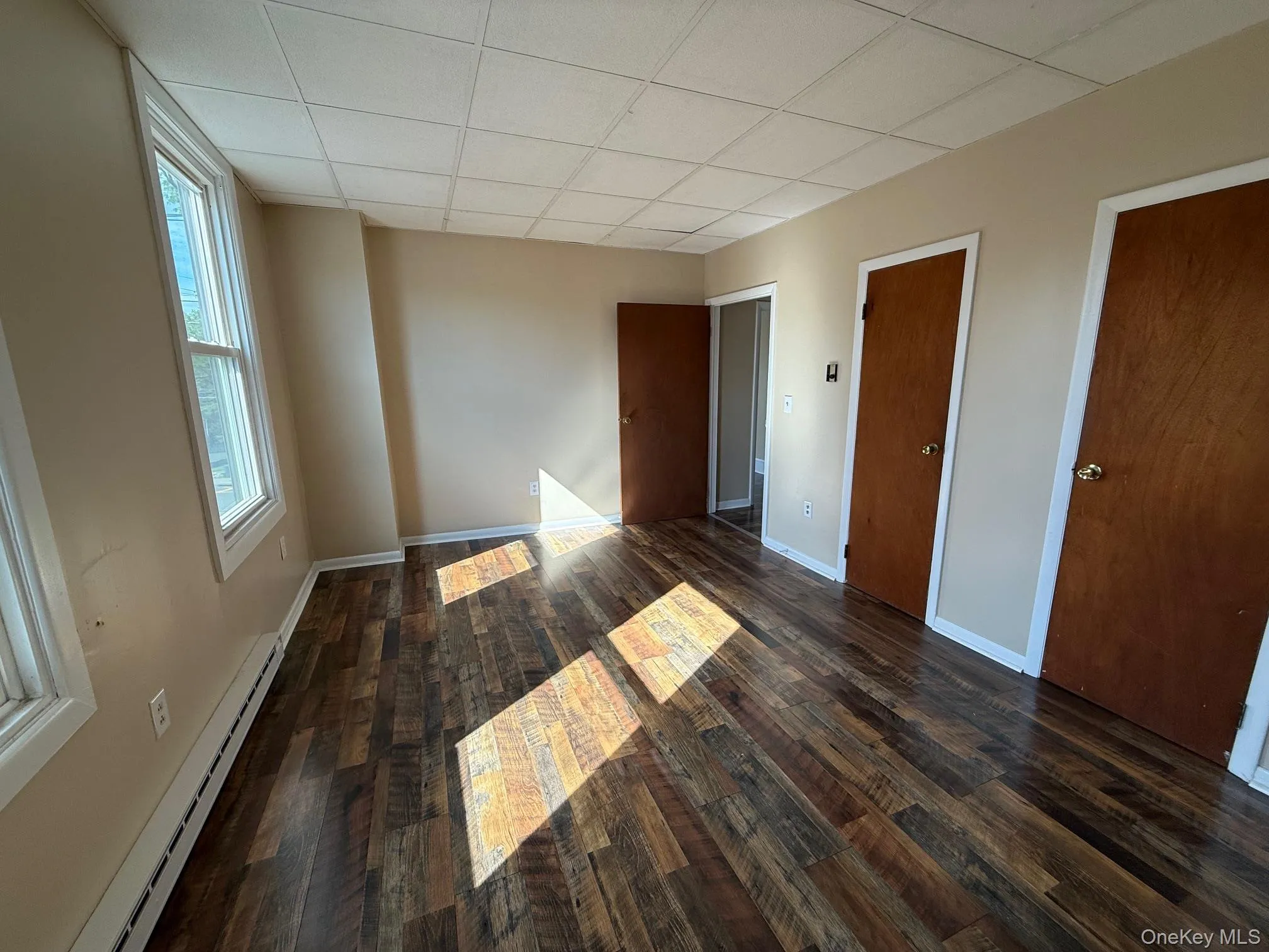 Unfurnished bedroom with baseboard heating, a drop ceiling, and wood finished floors Unfurnished bedroom with baseboard heating, a drop ceiling, and wood finished floors