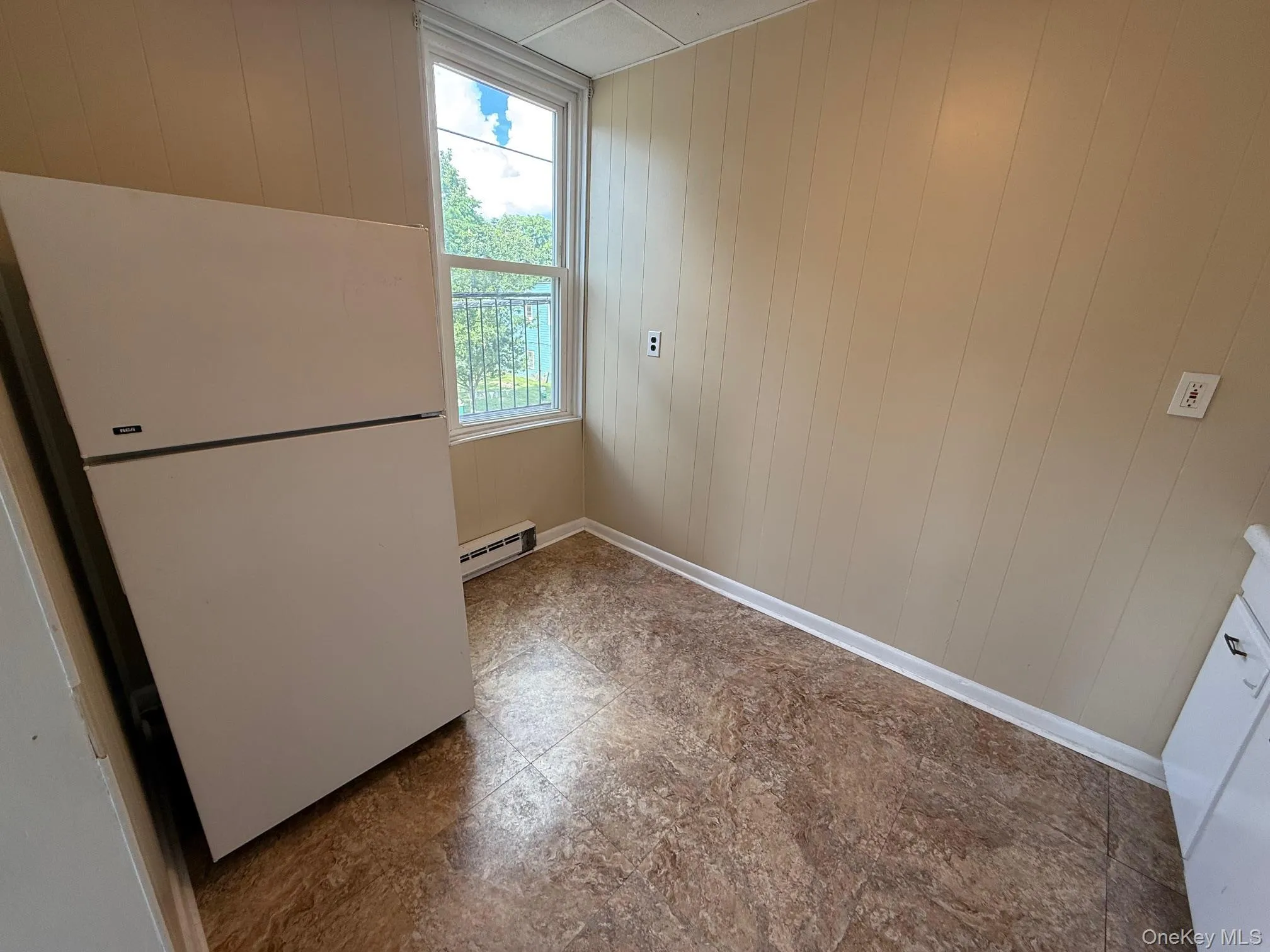 Empty room featuring wooden walls, a baseboard radiator, and tile patterned floors Empty room featuring wooden walls, a baseboard radiator, and tile patterned floors