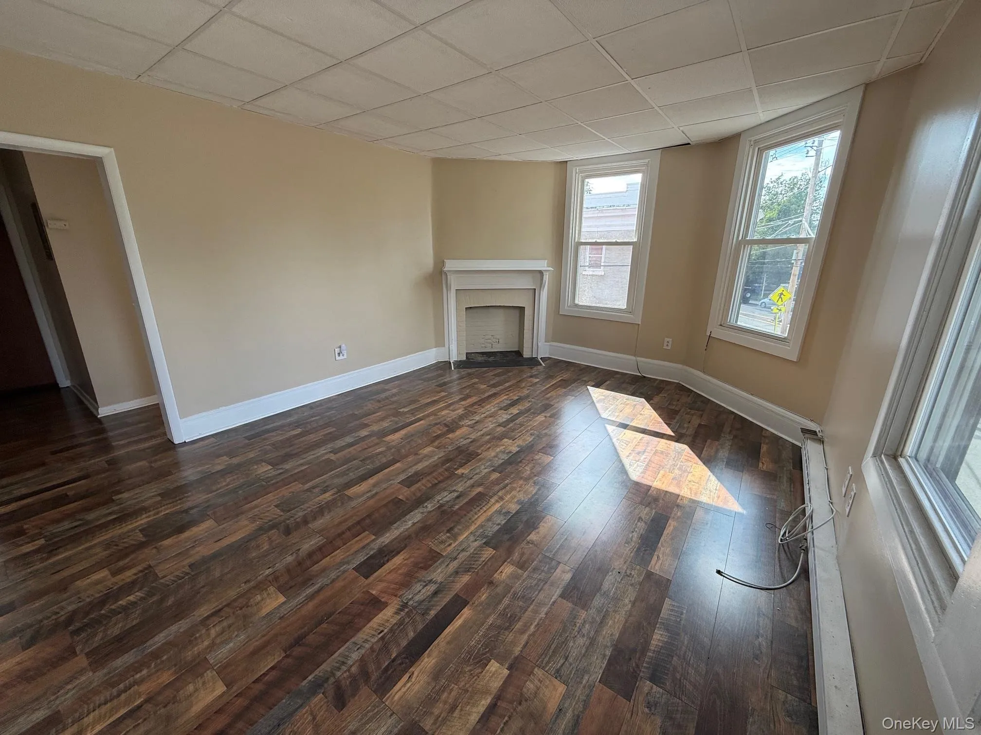 Unfurnished living room with a drop ceiling, dark wood-style flooring, and a fireplace Unfurnished living room with a drop ceiling, dark wood-style flooring, and a fireplace