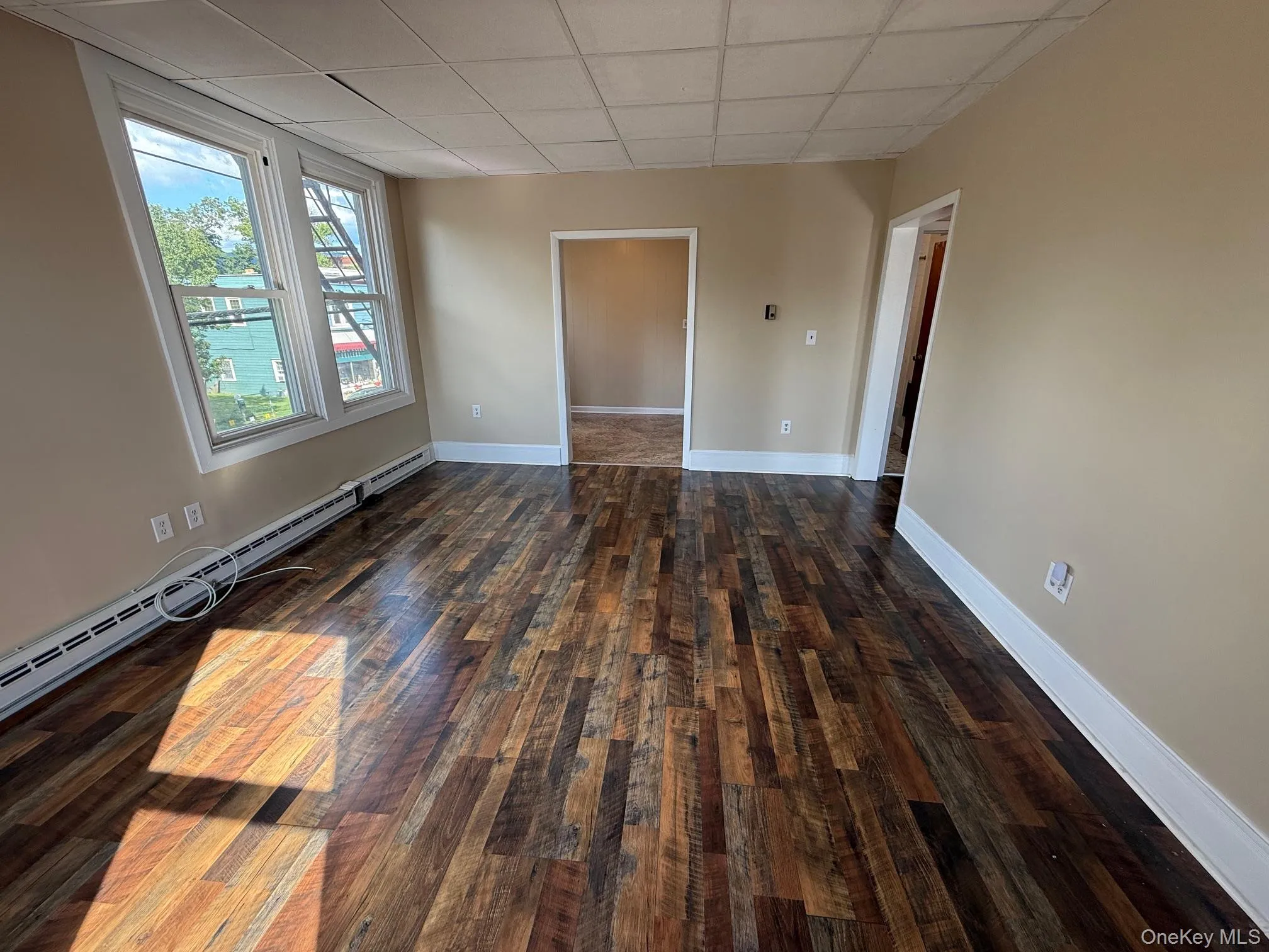 Unfurnished room featuring a paneled ceiling, a baseboard radiator, and dark wood-type flooring Unfurnished room featuring a paneled ceiling, a baseboard radiator, and dark wood-type flooring