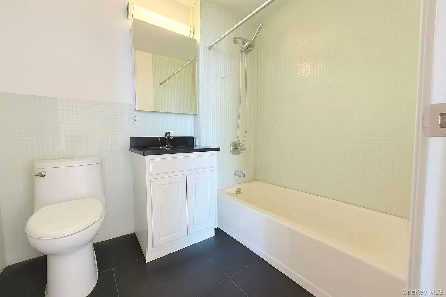 Bathroom featuring bathtub / shower combination, tile walls, dark tile patterned flooring, vanity, and a wainscoted wall Bathroom featuring bathtub / shower combination, tile walls, dark tile patterned flooring, vanity, and a wainscoted wall