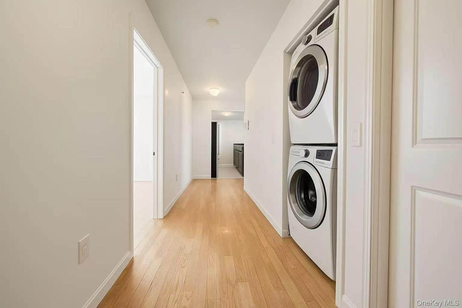 Washroom featuring light wood finished floors and stacked washer / dryer Washroom featuring light wood finished floors and stacked washer / dryer