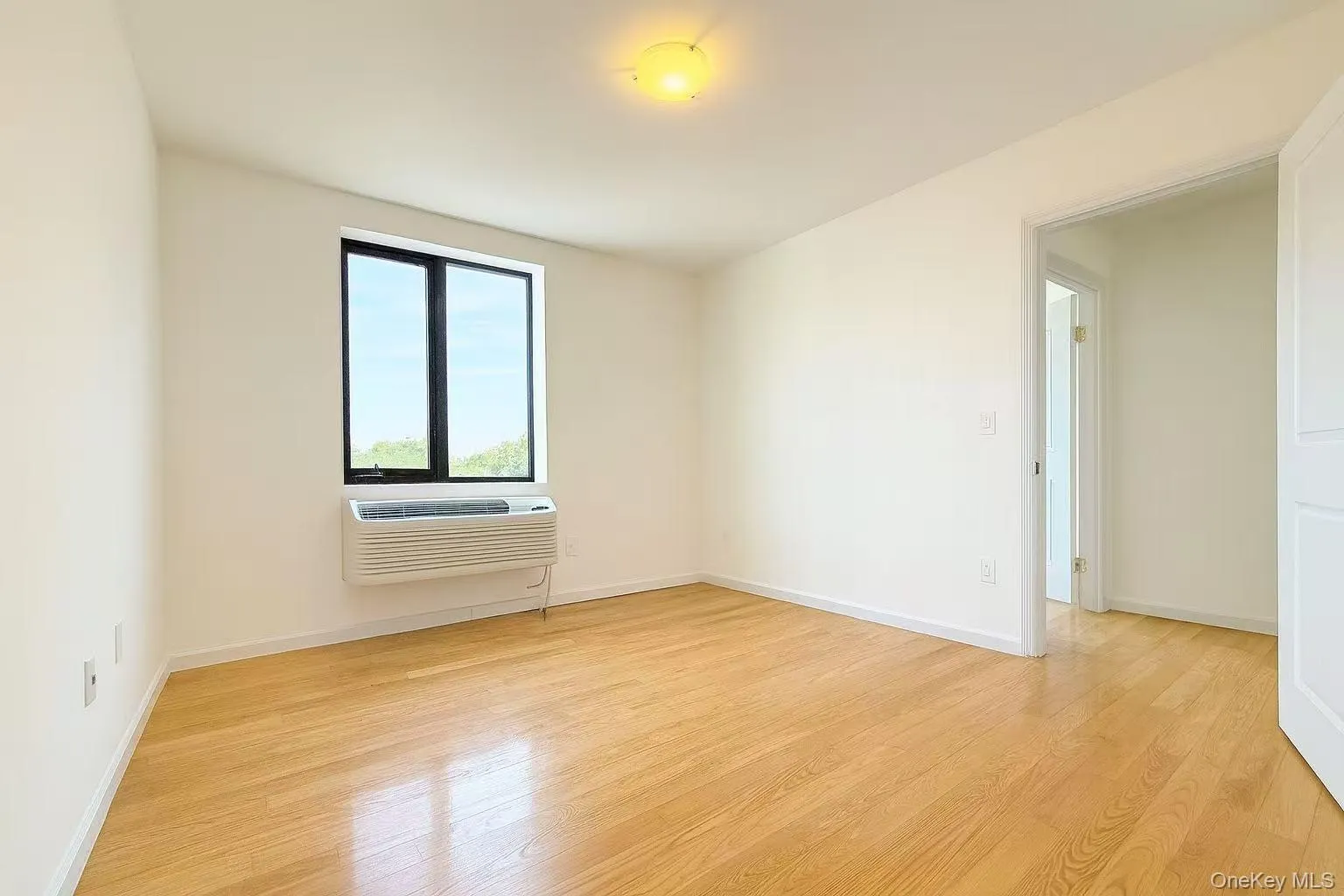 Empty room with light wood-type flooring and an AC wall unit Empty room with light wood-type flooring and an AC wall unit