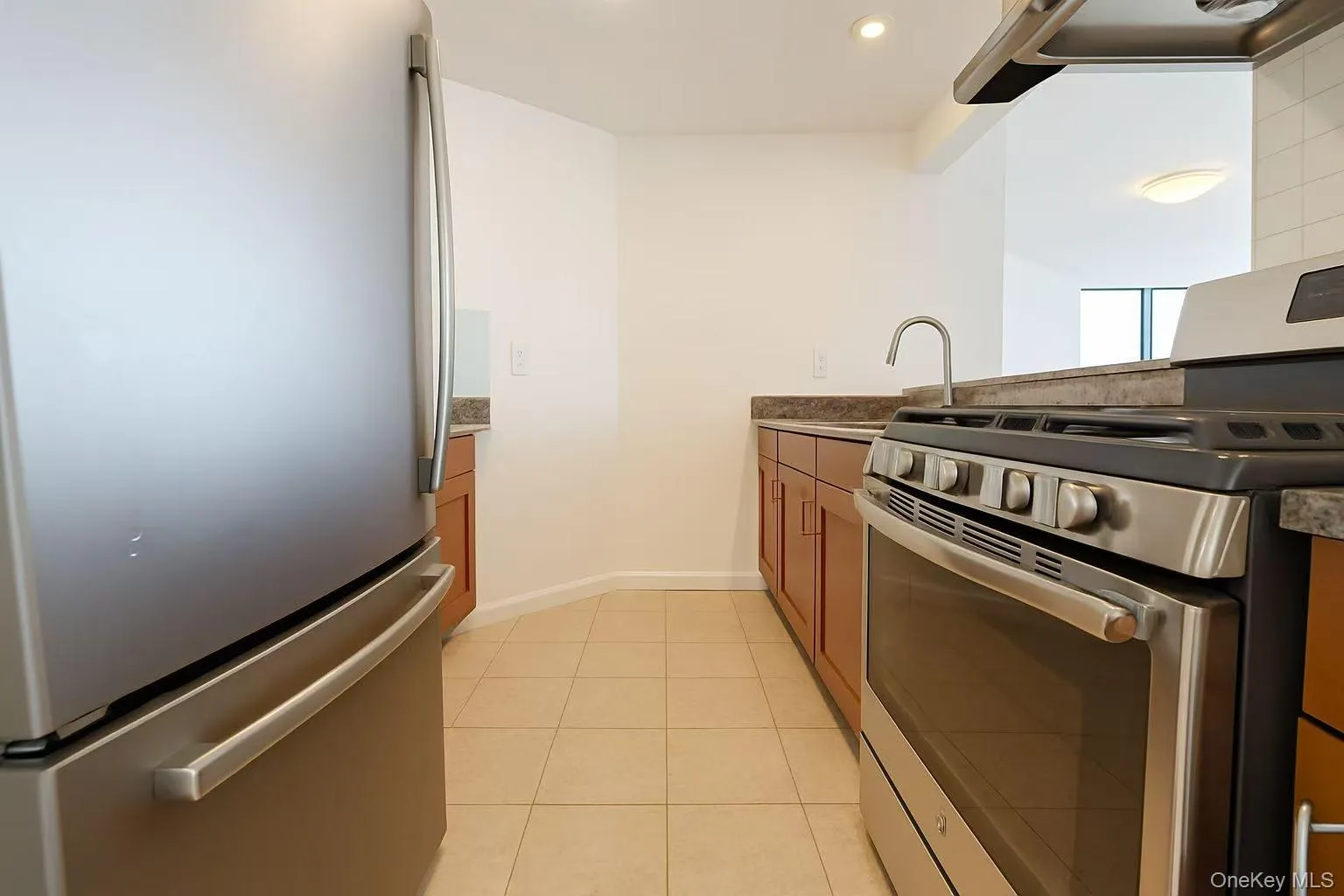 Kitchen with appliances with stainless steel finishes, light tile patterned floors, brown cabinetry, ventilation hood, and a peninsula Kitchen with appliances with stainless steel finishes, light tile patterned floors, brown cabinetry, ventilation hood, and a peninsula