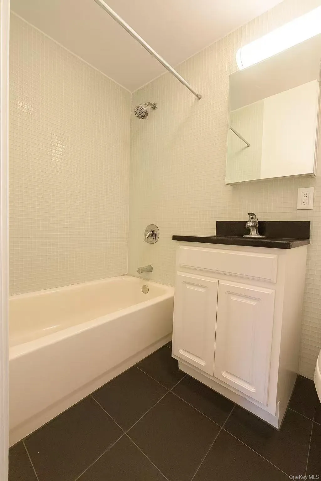 Bathroom with shower / tub combination, dark tile patterned floors, vanity, and tile walls Bathroom with shower / tub combination, dark tile patterned floors, vanity, and tile walls