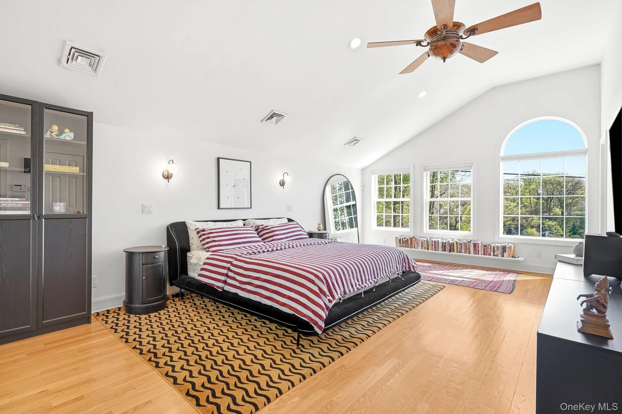 Vaulted ceiling bedroom featuring hardwood flooring, a ceiling fan, and multiple wall sconces Vaulted ceiling bedroom featuring hardwood flooring, a ceiling fan, and multiple wall sconces