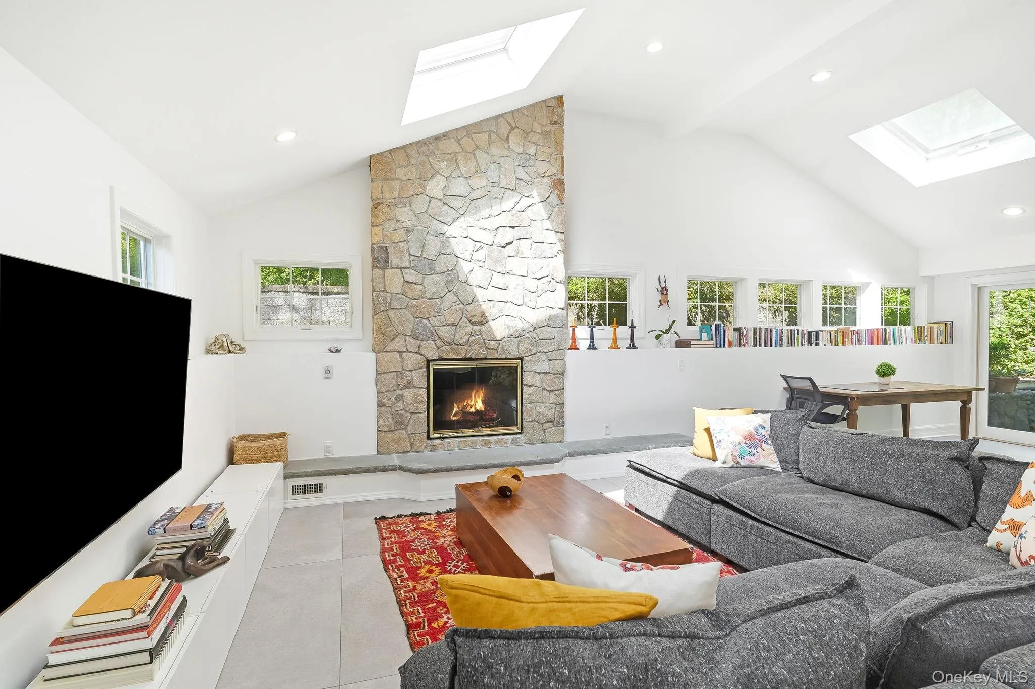 Oversized living room featuring a stone wood -burning fireplace with hearth, vaulted ceilings, and skylights Oversized living room featuring a stone wood -burning fireplace with hearth, vaulted ceilings, and skylights