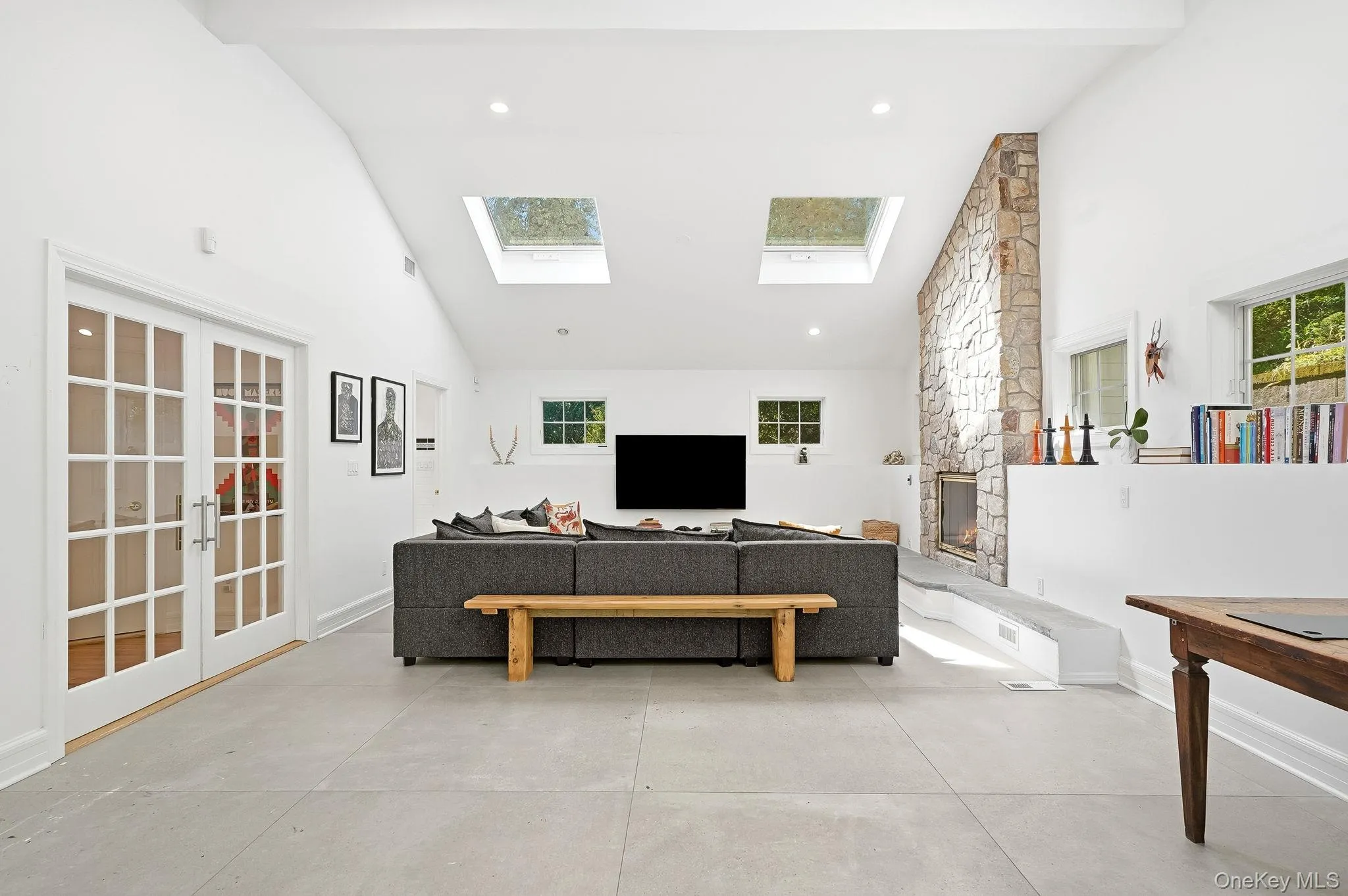 Spacious living area featuring a vaulted ceiling with two skylights, a floor-to-ceiling stone fireplace, and light-toned concrete flooring Spacious living area featuring a vaulted ceiling with two skylights, a floor-to-ceiling stone fireplace, and light-toned concrete flooring