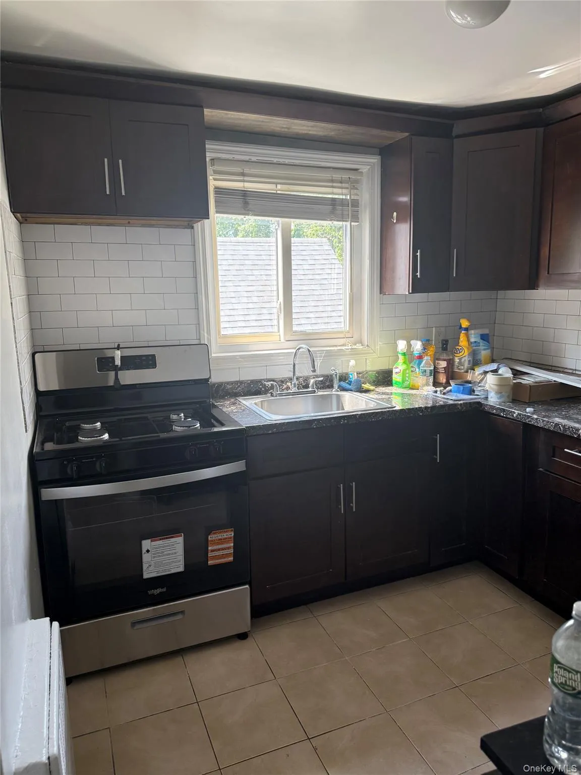 Kitchen with stainless steel stove, light tile patterned floors, decorative backsplash, and dark countertops Kitchen with stainless steel stove, light tile patterned floors, decorative backsplash, and dark countertops