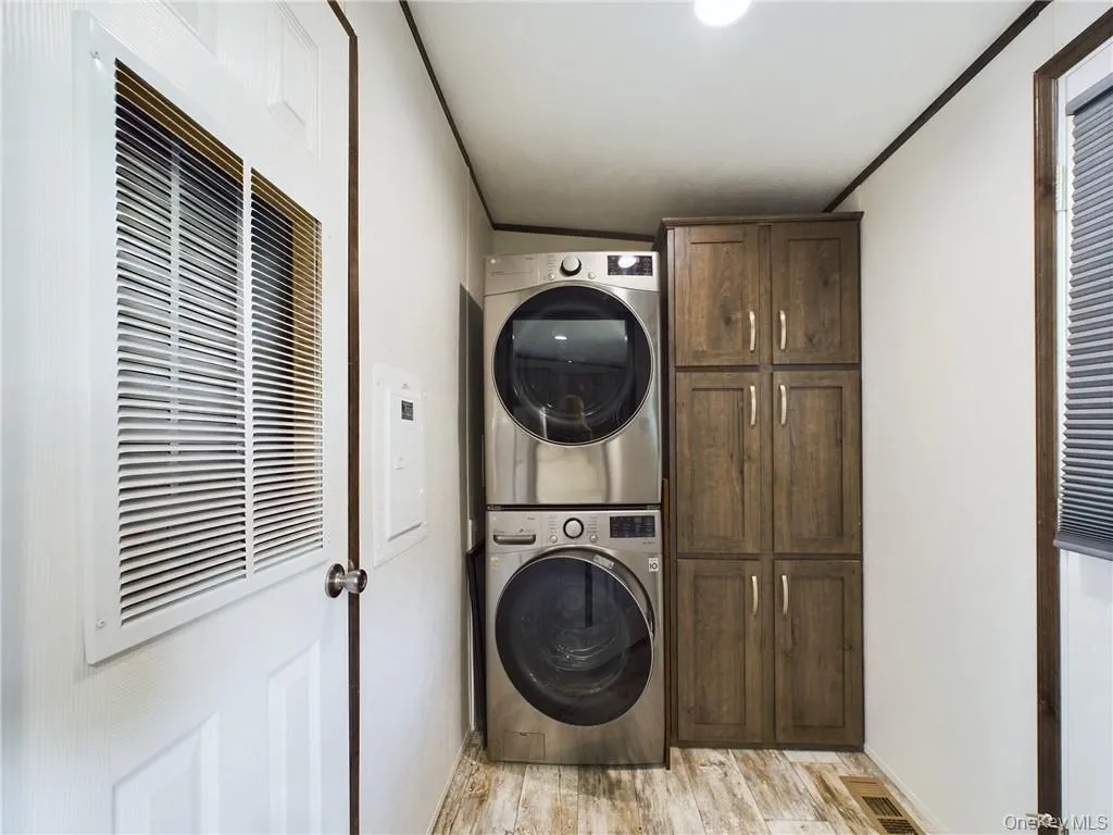 Clothes washing area featuring light hardwood / wood-style flooring, stacked washer and clothes dryer, and cabinets Clothes washing area featuring light hardwood / wood-style flooring, stacked washer and clothes dryer, and cabinets
