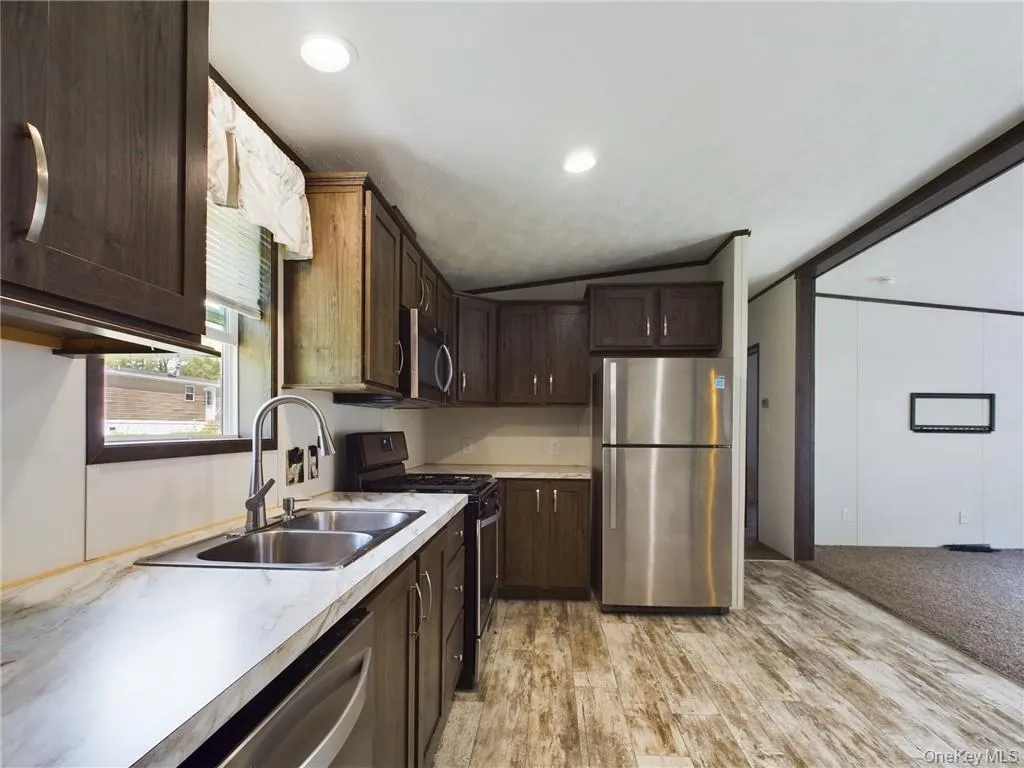 Kitchen featuring dark brown cabinets, light colored carpet, appliances with stainless steel finishes, sink, and lofted ceiling Kitchen featuring dark brown cabinets, light colored carpet, appliances with stainless steel finishes, sink, and lofted ceiling