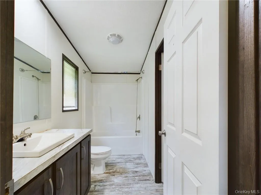 Full bathroom with hardwood / wood-style flooring, vanity, toilet, and shower / bathtub combination Full bathroom with hardwood / wood-style flooring, vanity, toilet, and shower / bathtub combination