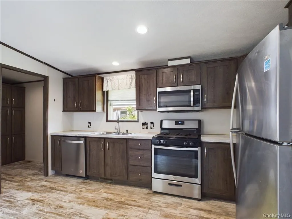 Kitchen with appliances with stainless steel finishes, light wood-type flooring, dark brown cabinetry, sink, and ornamental molding Kitchen with appliances with stainless steel finishes, light wood-type flooring, dark brown cabinetry, sink, and ornamental molding