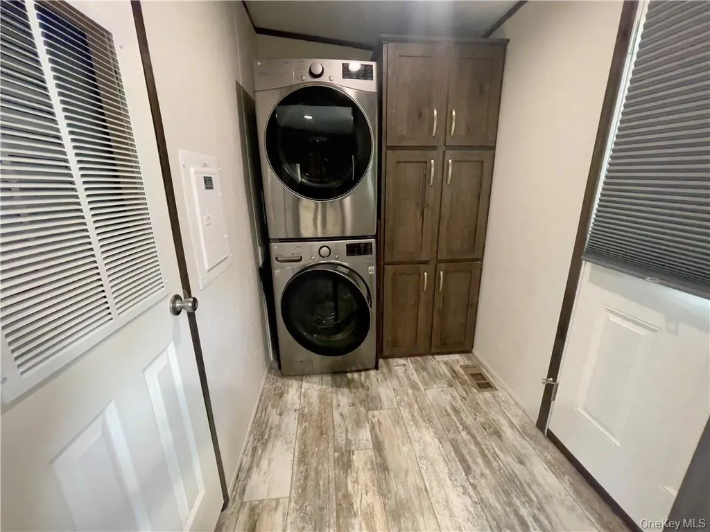 Laundry room with stacked washer and clothes dryer, cabinets, and light wood-type flooring Laundry room with stacked washer and clothes dryer, cabinets, and light wood-type flooring