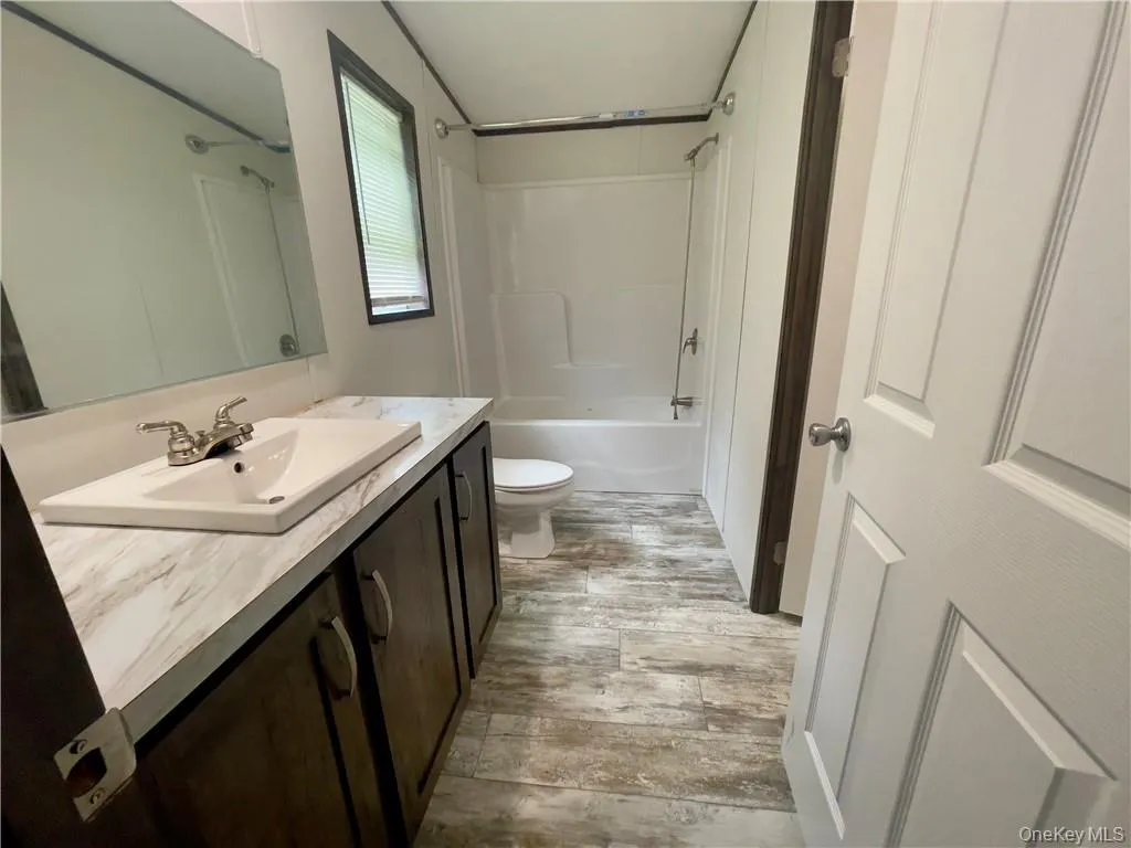 Full bathroom with wood-type flooring, oversized vanity, toilet, and tub / shower combination Full bathroom with wood-type flooring, oversized vanity, toilet, and tub / shower combination