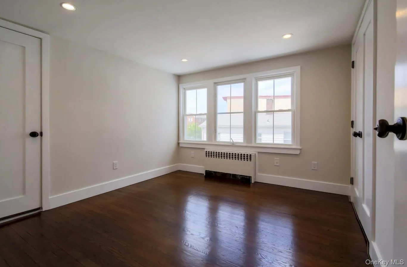 Empty room with radiator heating unit, dark wood-style flooring, and recessed lighting Empty room with radiator heating unit, dark wood-style flooring, and recessed lighting