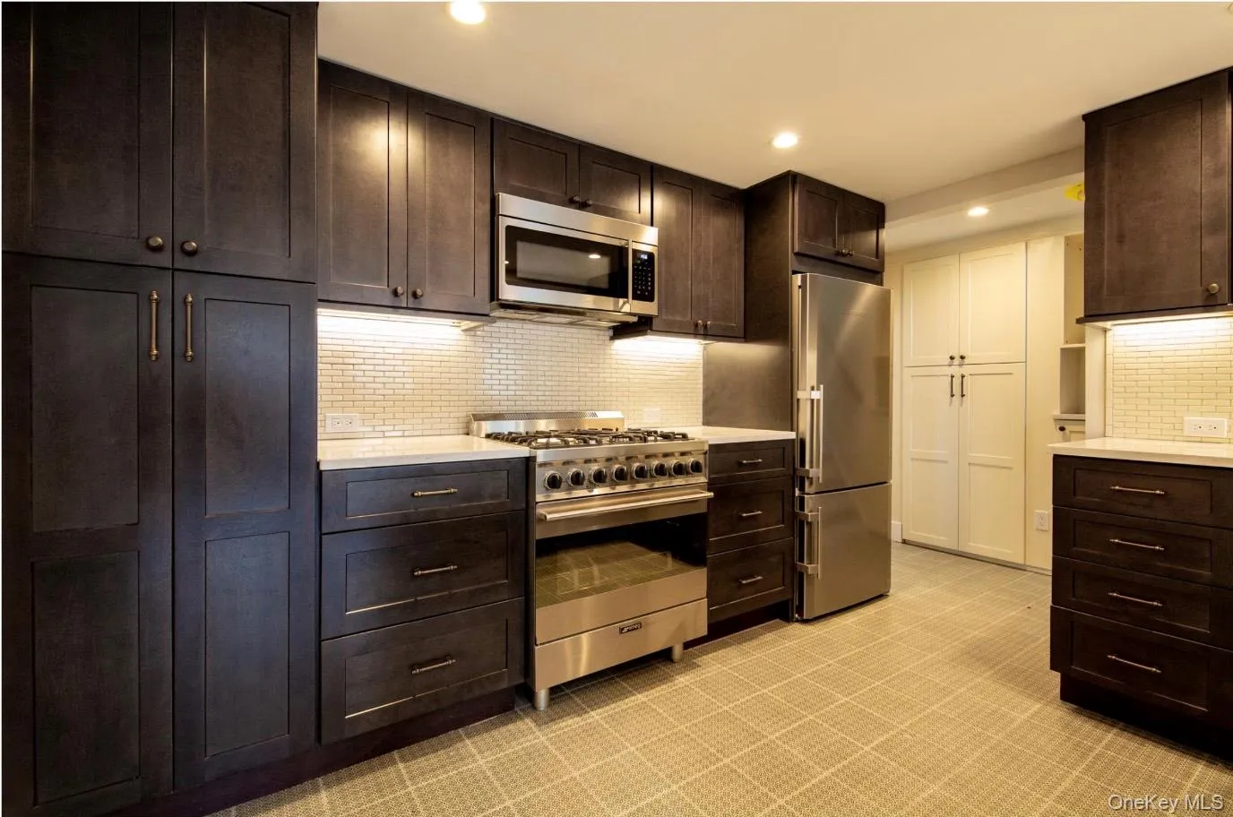 Kitchen with premium appliances, light countertops, decorative backsplash, recessed lighting, and dark brown cabinetry Kitchen with premium appliances, light countertops, decorative backsplash, recessed lighting, and dark brown cabinetry