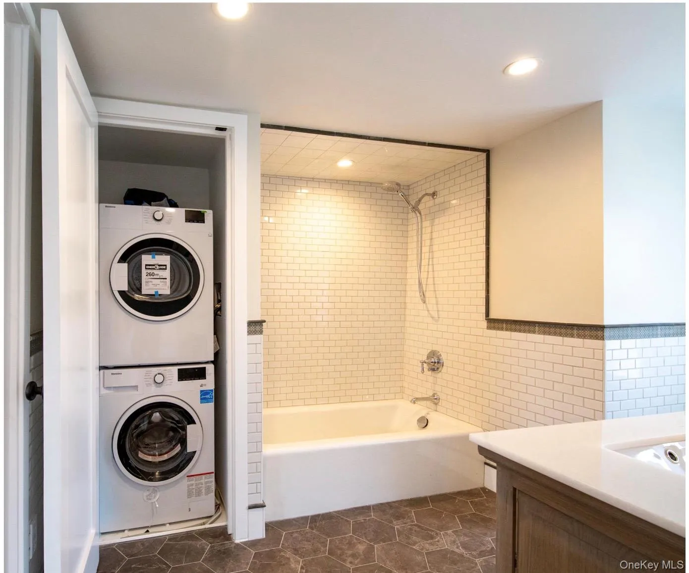 Bathroom featuring stacked washer / dryer, shower / washtub combination, recessed lighting, vanity, and tile walls Bathroom featuring stacked washer / dryer, shower / washtub combination, recessed lighting, vanity, and tile walls