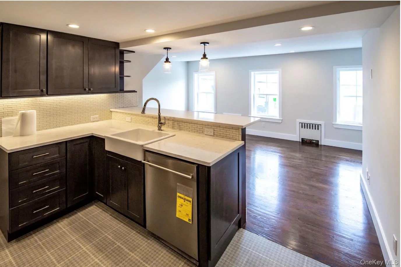 Kitchen featuring stainless steel dishwasher, radiator heating unit, a peninsula, backsplash, and dark brown cabinets Kitchen featuring stainless steel dishwasher, radiator heating unit, a peninsula, backsplash, and dark brown cabinets