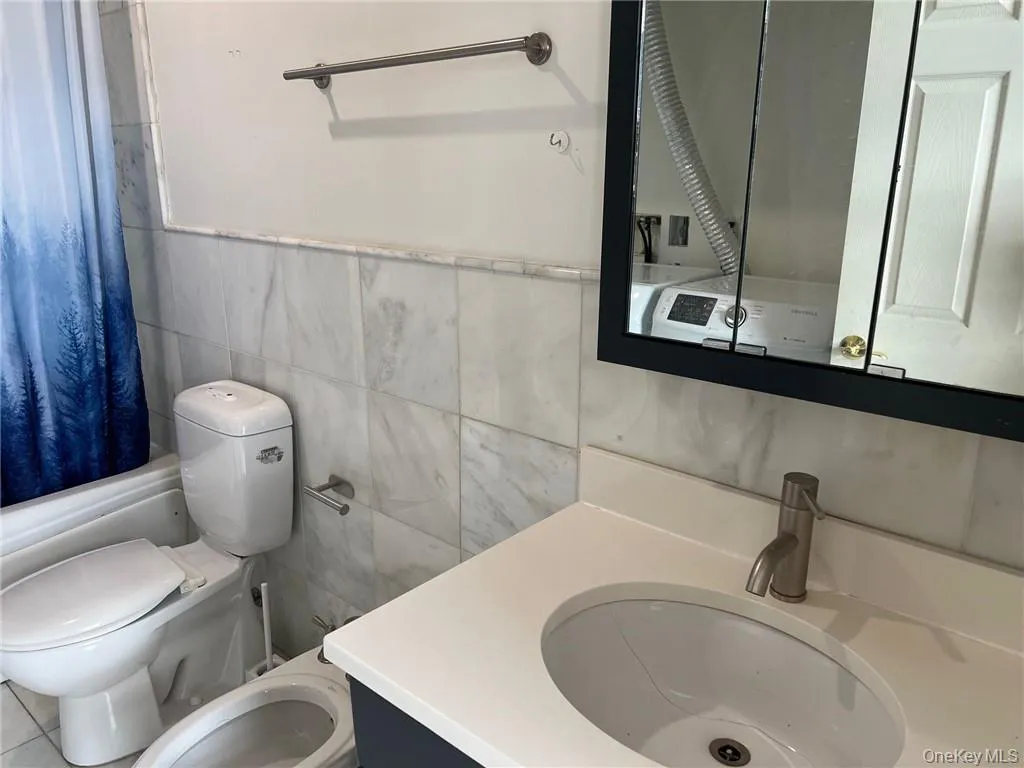 Full bathroom with shower / tub combo, tile walls, vanity, and toilet Full bathroom with shower / tub combo, tile walls, vanity, and toilet