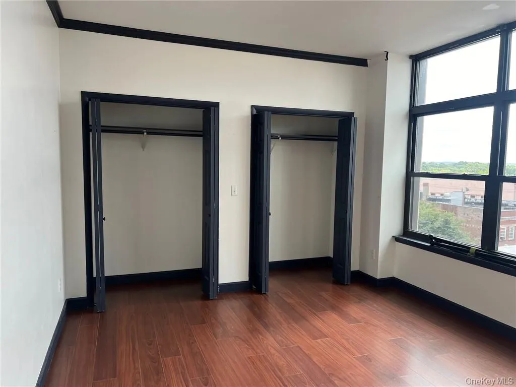 Unfurnished bedroom with ornamental molding, two closets, and dark wood-type flooring Unfurnished bedroom with ornamental molding, two closets, and dark wood-type flooring
