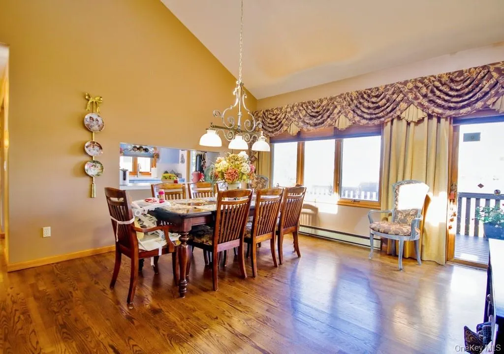 Dining room featuring wood finished floors, high vaulted ceiling, a baseboard radiator, and a chandelier Dining room featuring wood finished floors, high vaulted ceiling, a baseboard radiator, and a chandelier