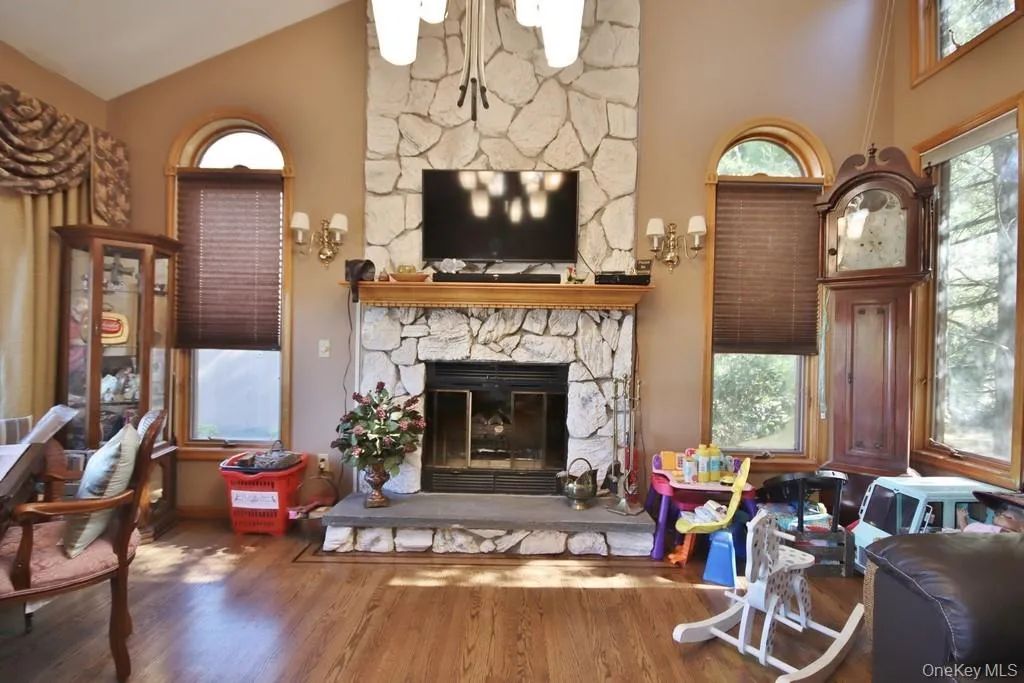 Living room with plenty of natural light, wood finished floors, high vaulted ceiling, and a stone fireplace Living room with plenty of natural light, wood finished floors, high vaulted ceiling, and a stone fireplace
