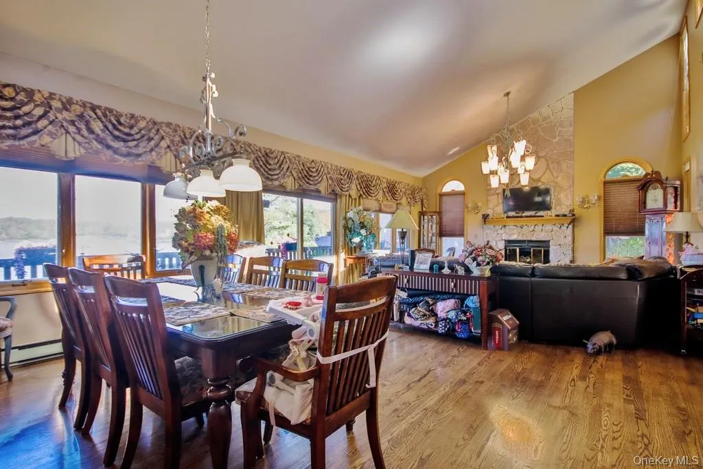 Dining area featuring wood finished floors, high vaulted ceiling, a chandelier, a fireplace, and a baseboard radiator Dining area featuring wood finished floors, high vaulted ceiling, a chandelier, a fireplace, and a baseboard radiator