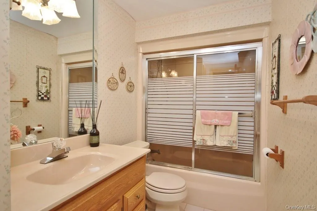 Bathroom with wallpapered walls, vanity, enclosed tub / shower combo, and tile patterned flooring Bathroom with wallpapered walls, vanity, enclosed tub / shower combo, and tile patterned flooring