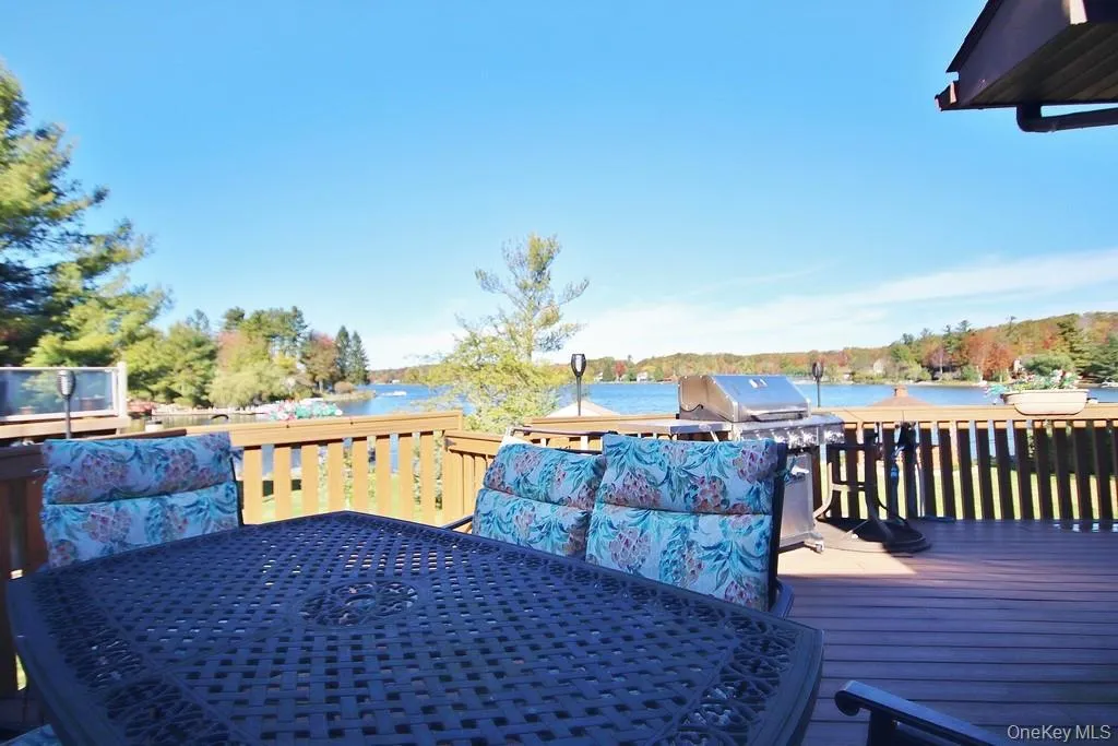Wooden terrace featuring outdoor dining area, grilling area, and a water view Wooden terrace featuring outdoor dining area, grilling area, and a water view