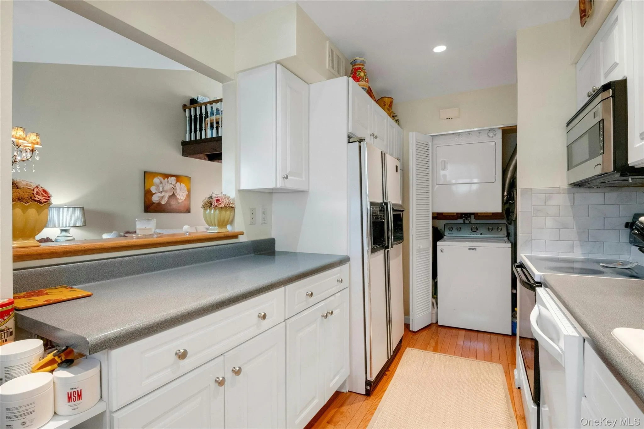 Kitchen featuring white cabinetry, gray countertops, refrigerator, and subway tile backsplash Kitchen featuring white cabinetry, gray countertops, refrigerator, and subway tile backsplash