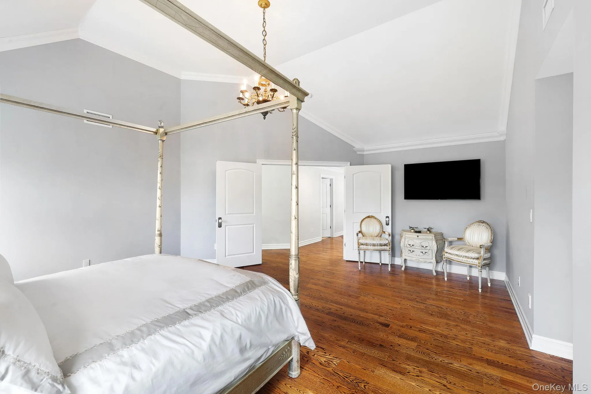Hardwood flooring, vaulted ceiling, crown molding, white paneled doors, and a gold-tone chandelier Hardwood flooring, vaulted ceiling, crown molding, white paneled doors, and a gold-tone chandelier