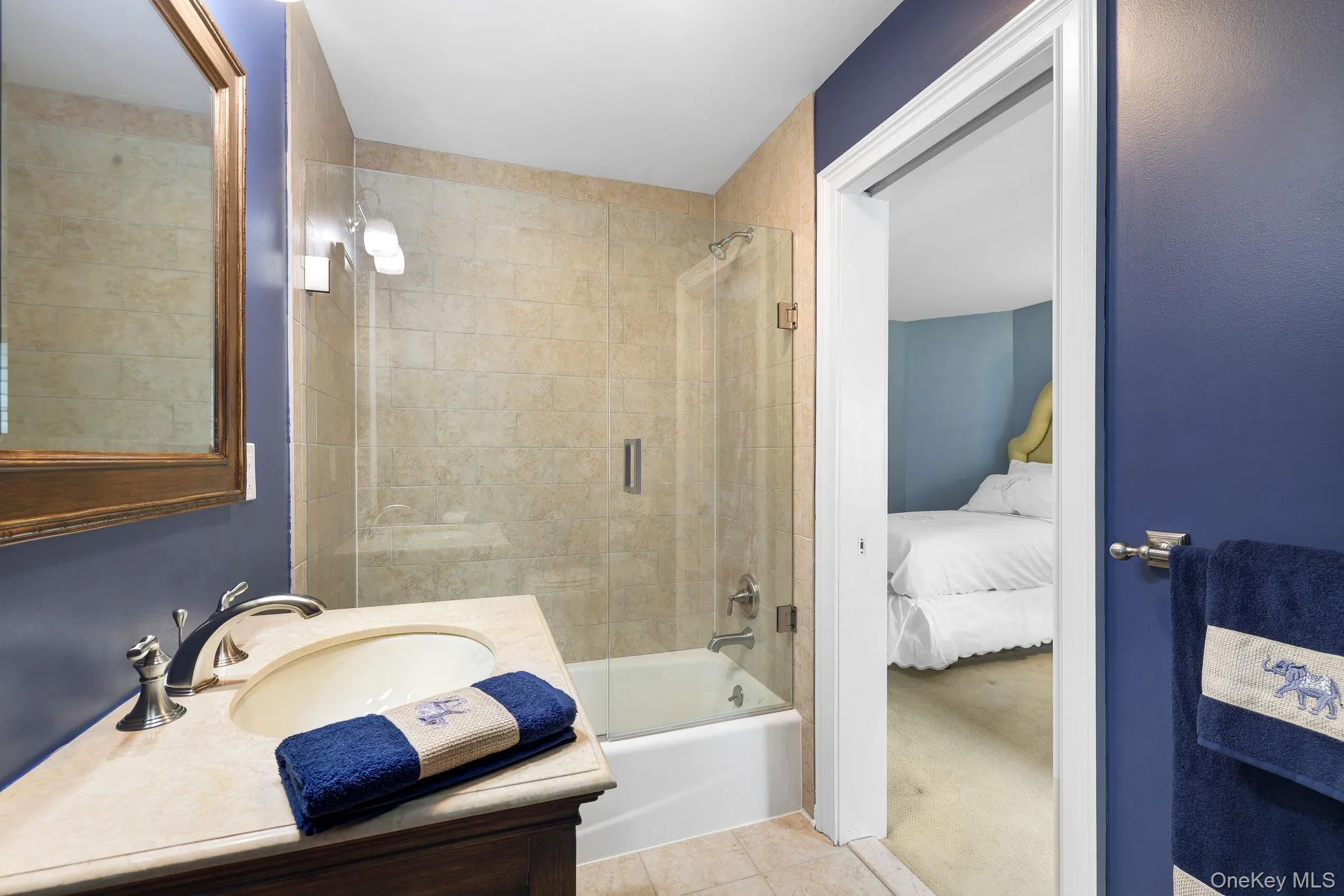 Jack and Jill bathroom featuring a single vanity with an integrated sink, polished chrome faucet, a framed mirror, and a tiled shower-tub combination with a glass enclosure Jack and Jill bathroom featuring a single vanity with an integrated sink, polished chrome faucet, a framed mirror, and a tiled shower-tub combination with a glass enclosure