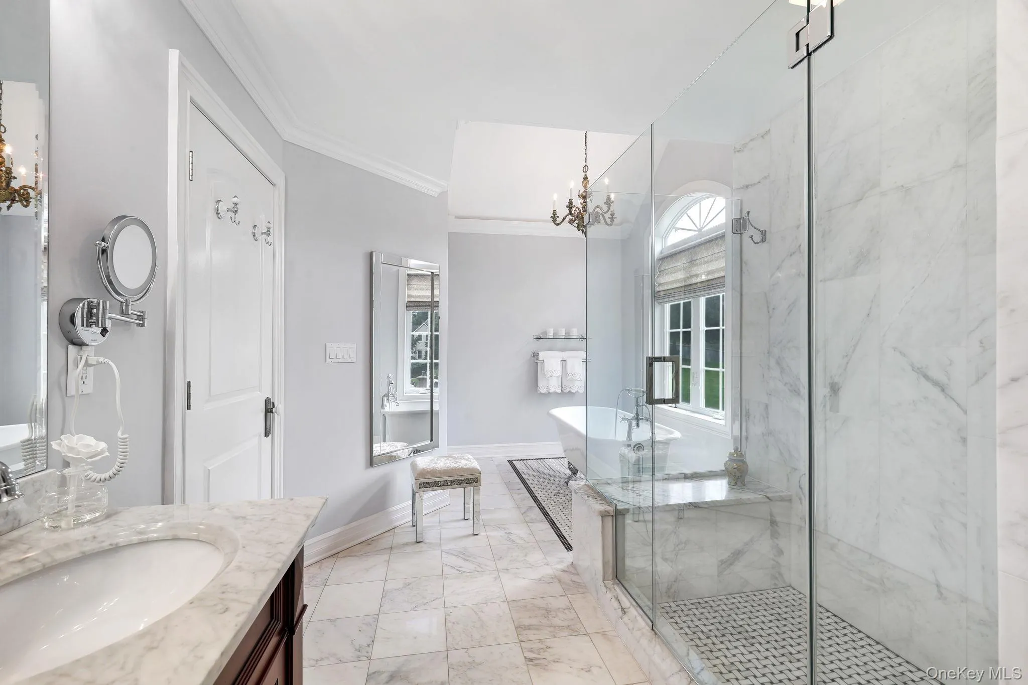 Marble-finish flooring, glass-enclosed shower with tile base, freestanding bathtub, and a double-hung arched window Marble-finish flooring, glass-enclosed shower with tile base, freestanding bathtub, and a double-hung arched window