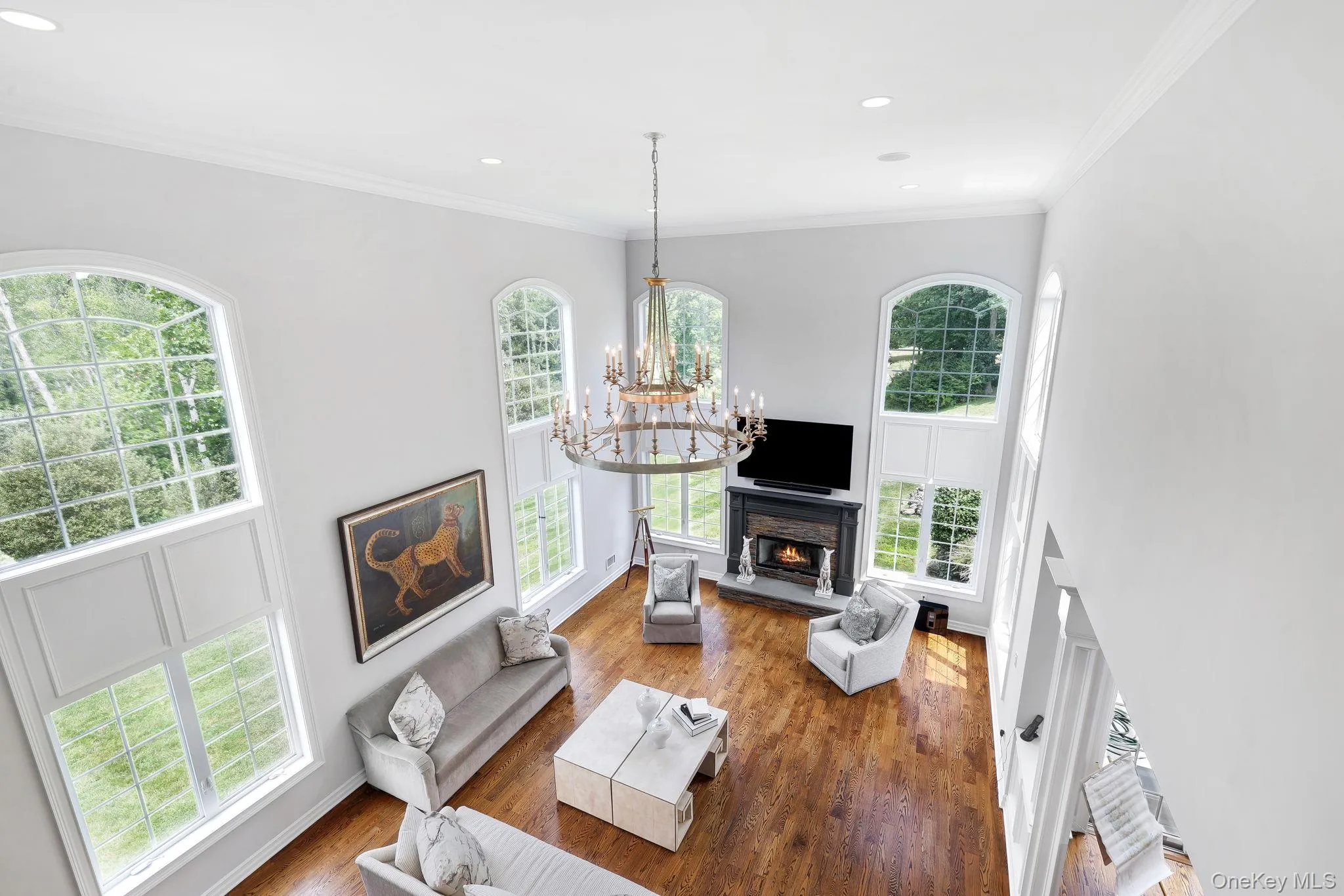 Two-story living area featuring hardwood flooring, a central chandelier, and a fireplace with a stone surround Two-story living area featuring hardwood flooring, a central chandelier, and a fireplace with a stone surround