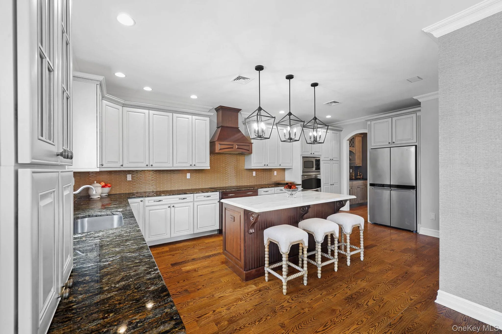 Kitchen featuring extensive white cabinetry, a central island with countertop, a stainless steel refrigerator, wood-finish flooring, and pendant lighting Kitchen featuring extensive white cabinetry, a central island with countertop, a stainless steel refrigerator, wood-finish flooring, and pendant lighting