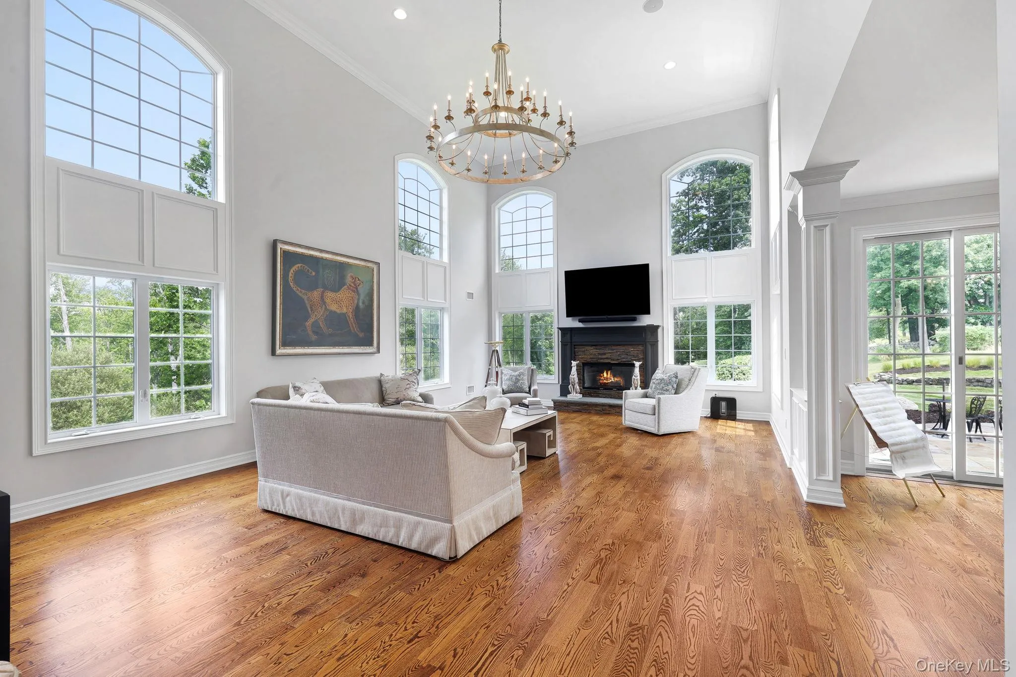 Vaulted ceiling with a large antique chandelier, wood-finish flooring, multiple arched windows, fireplace with a dark mantel, and sliding glass patio doors Vaulted ceiling with a large antique chandelier, wood-finish flooring, multiple arched windows, fireplace with a dark mantel, and sliding glass patio doors