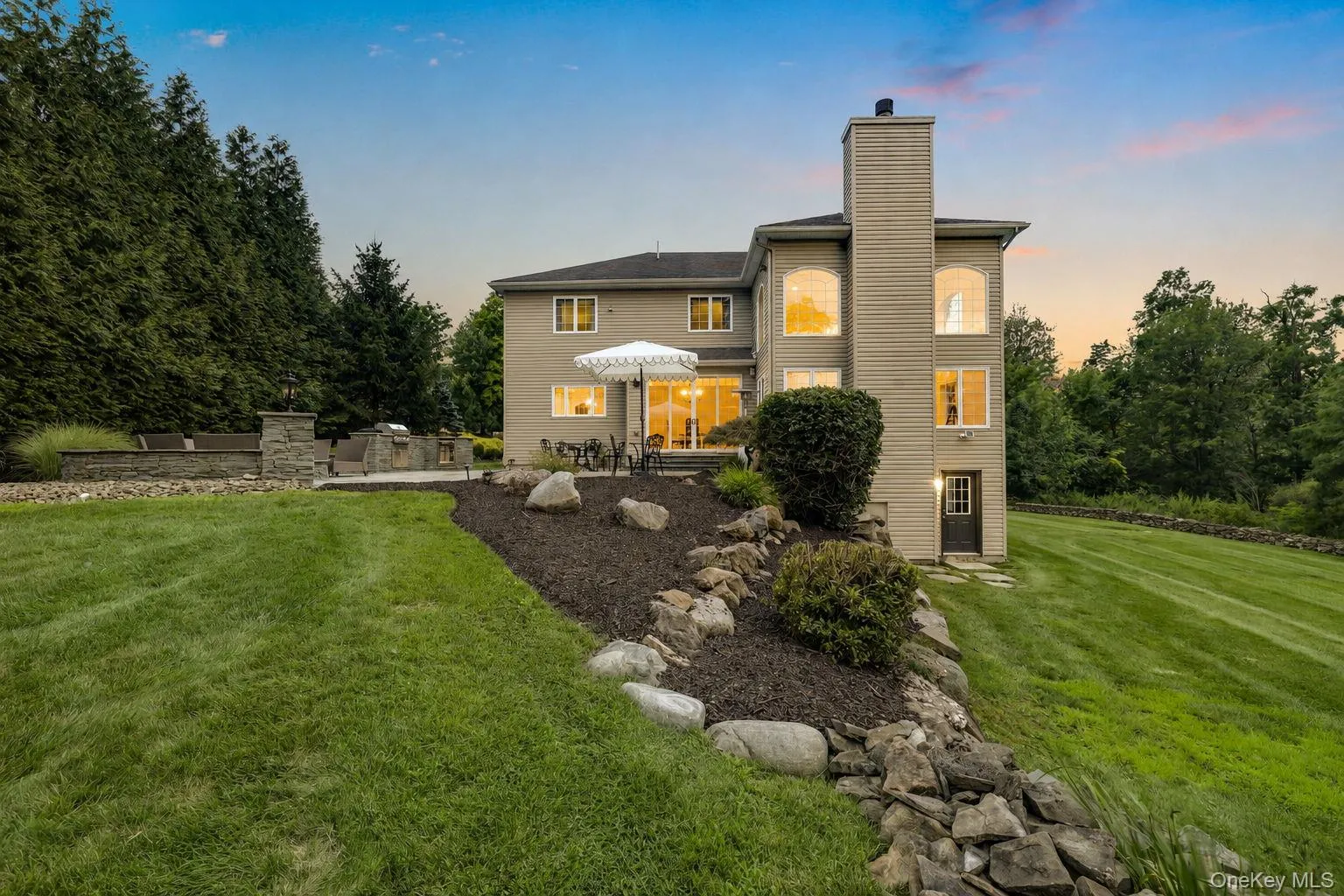 Rear exterior featuring multiple large windows, a stone-accented outdoor patio, and a dedicated outdoor cooking area Rear exterior featuring multiple large windows, a stone-accented outdoor patio, and a dedicated outdoor cooking area