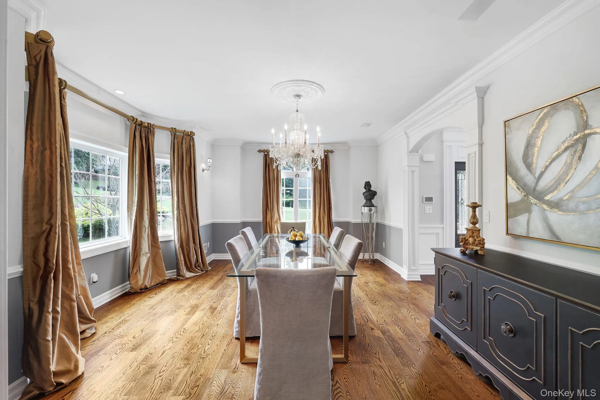 Hardwood flooring, arched doorway, elegant chandelier, crown molding, and wainscoting Hardwood flooring, arched doorway, elegant chandelier, crown molding, and wainscoting