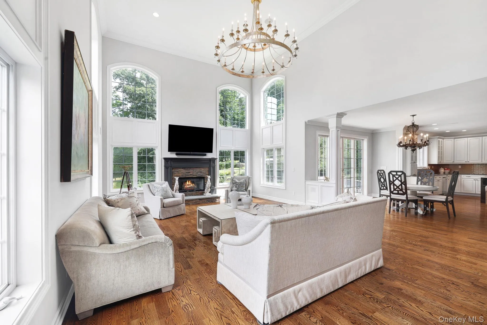 Two-story living area with hardwood flooring, a fireplace featuring a dark mantel, and multiple arched windows Two-story living area with hardwood flooring, a fireplace featuring a dark mantel, and multiple arched windows
