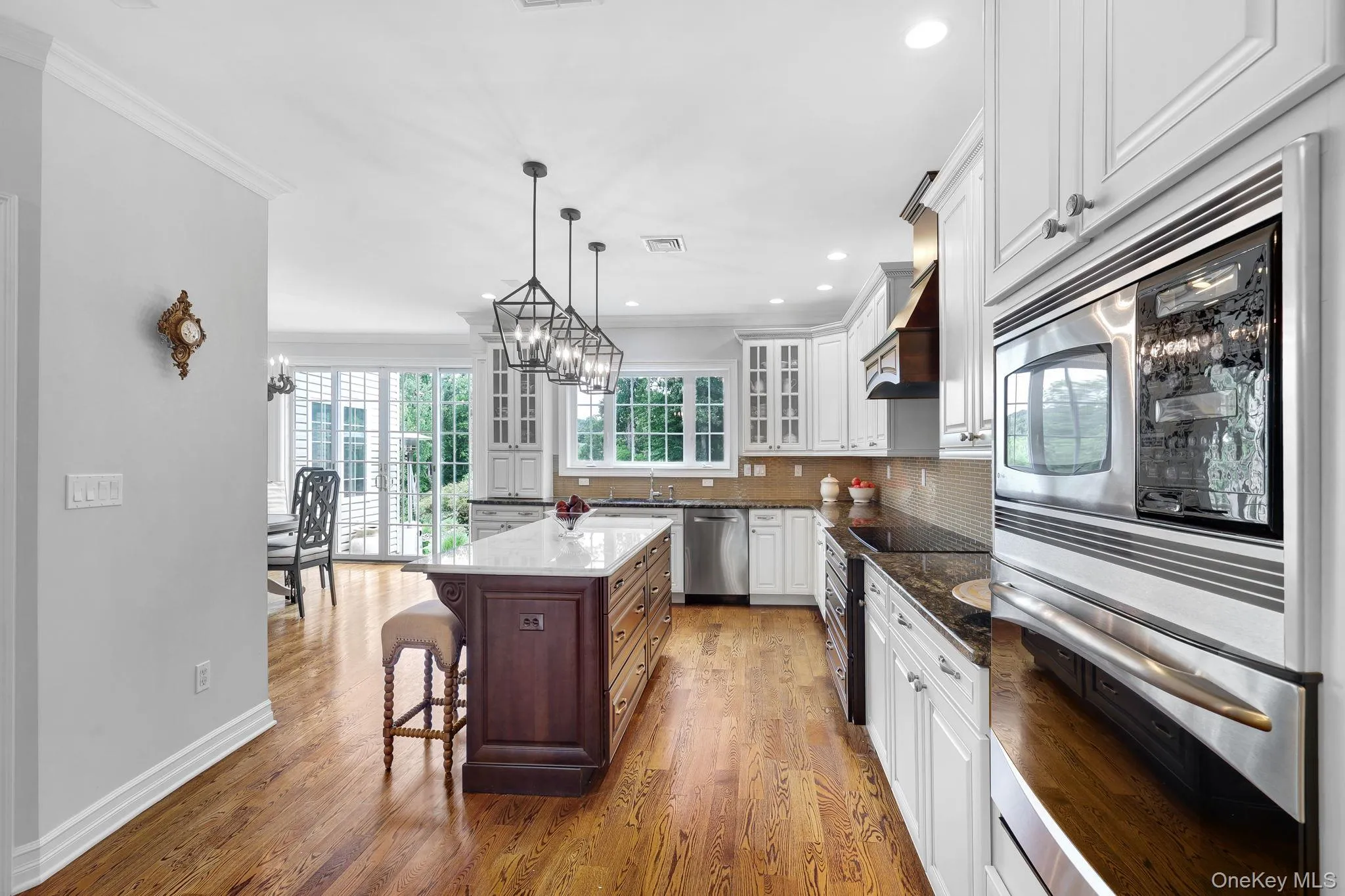 Kitchen featuring wood-finish flooring, white cabinetry, a dark wood-finish island with a light-toned countertop, and stainless steel built-in appliances Kitchen featuring wood-finish flooring, white cabinetry, a dark wood-finish island with a light-toned countertop, and stainless steel built-in appliances