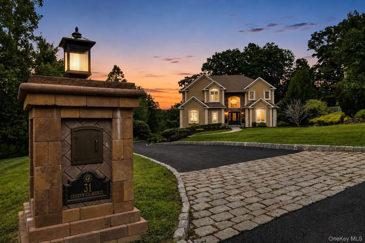 Belgium block curbing ,elegant custom stone and lighted mail box, custom pavers with evening view of two-story residence exterior with multiple illuminated windows Belgium block curbing ,elegant custom stone and lighted mail box, custom pavers with evening view of two-story residence exterior with multiple illuminated windows