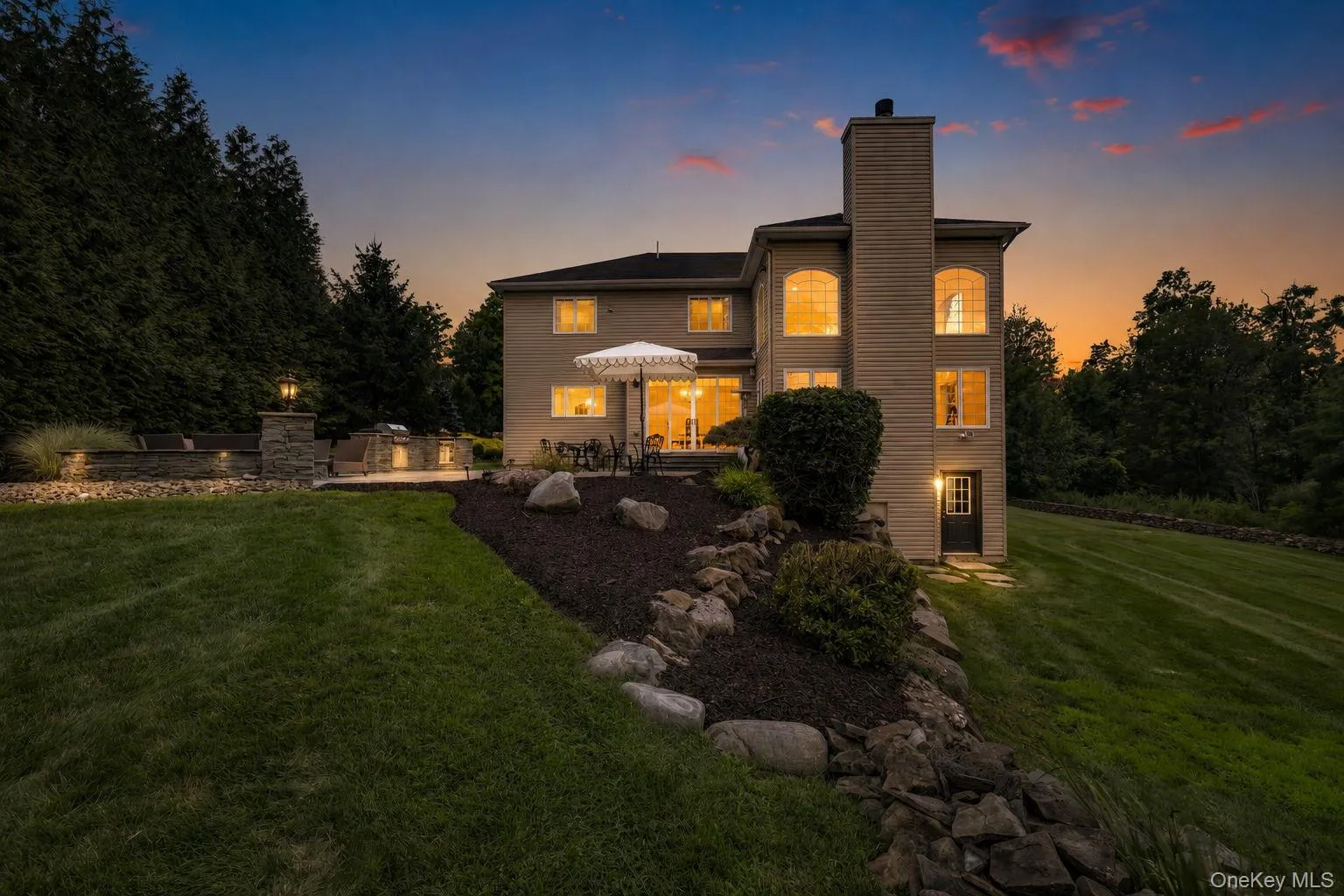 Extensive backyard with a manicured lawn, a stone retaining wall, and a multi-level patio featuring a built-in kitchen/grill station Extensive backyard with a manicured lawn, a stone retaining wall, and a multi-level patio featuring a built-in kitchen/grill station